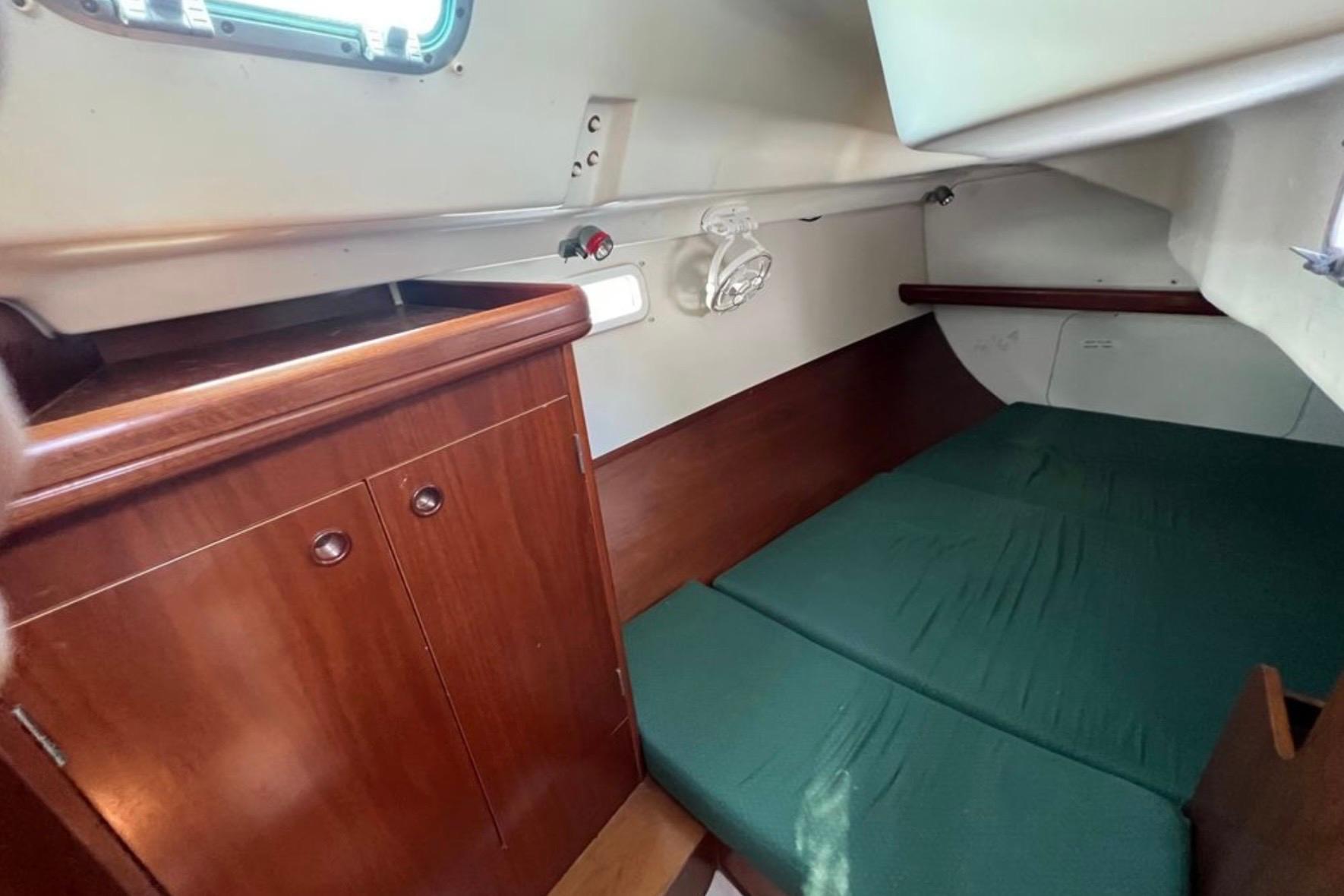 Cozy cabin interior of 2001 Beneteau 331 sailboat with wooden cabinetry and green bedding.