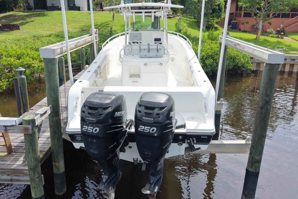 2018 Mako 284 Center Console boat with twin Mercury 250 engines docked by greenery.