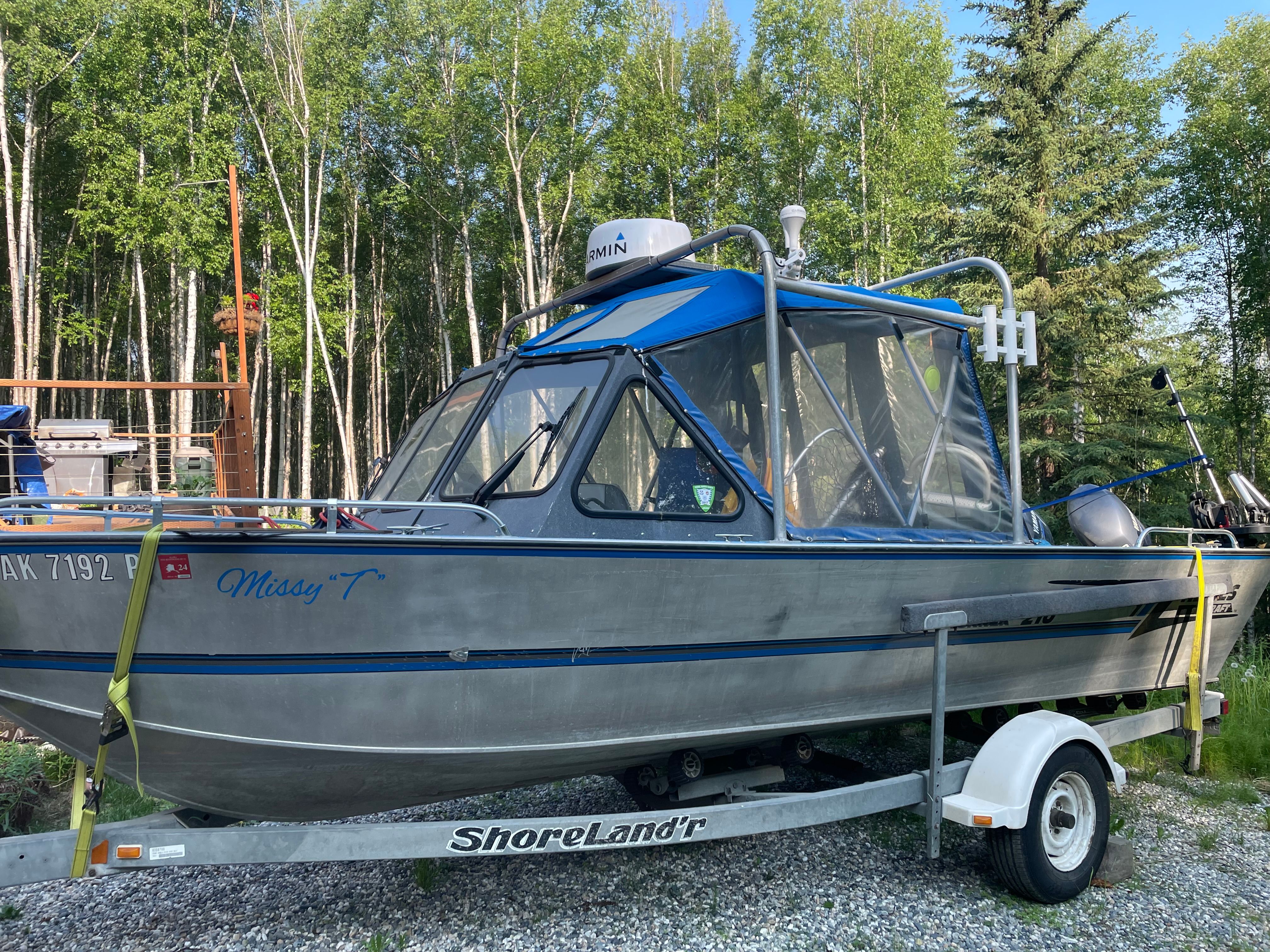 A Hewescraft Sea Runner 210 boat on a trailer, surrounded by trees.