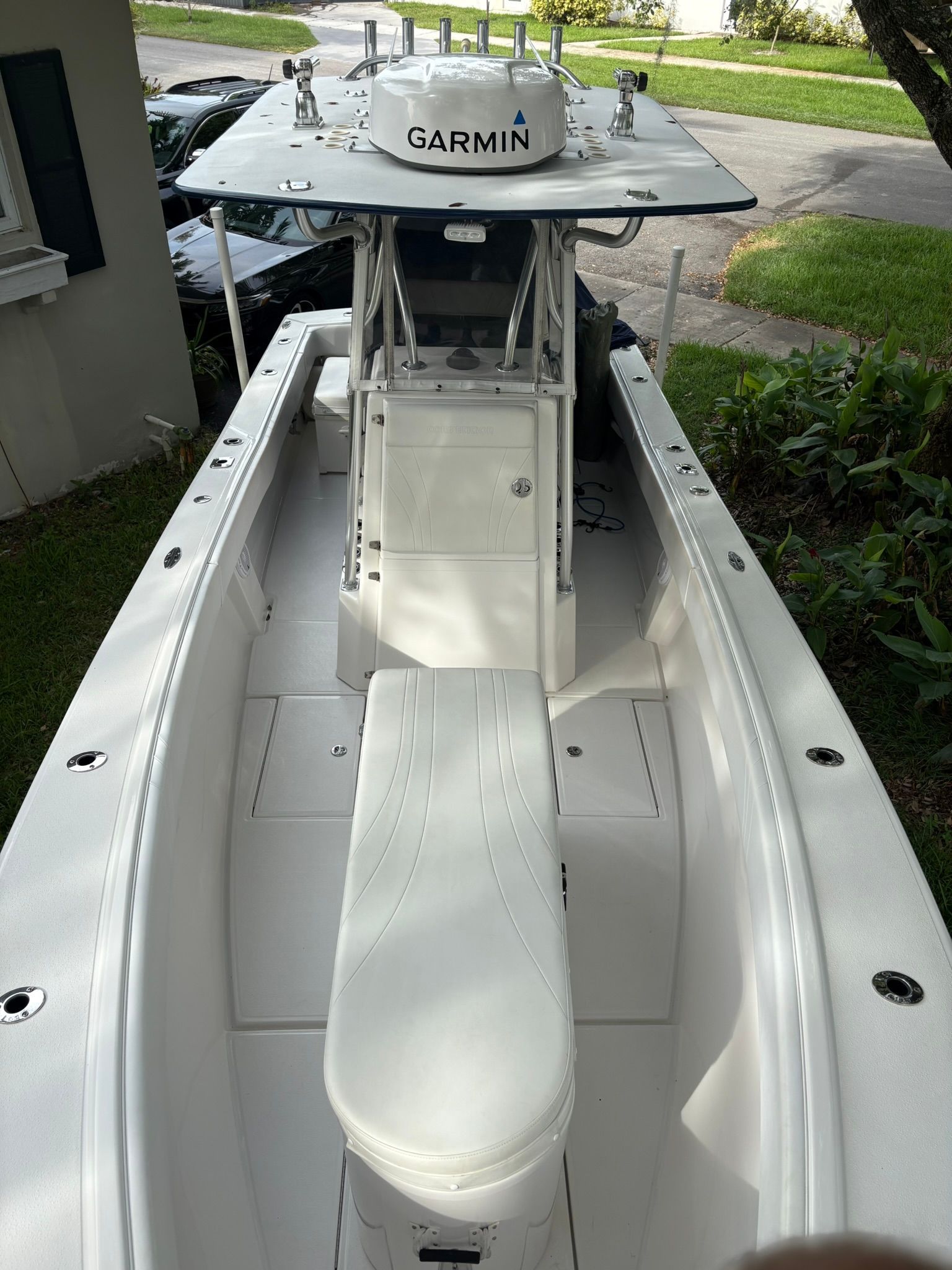 A white boat with a Garmin navigation system, parked on a trailer in a garden.
