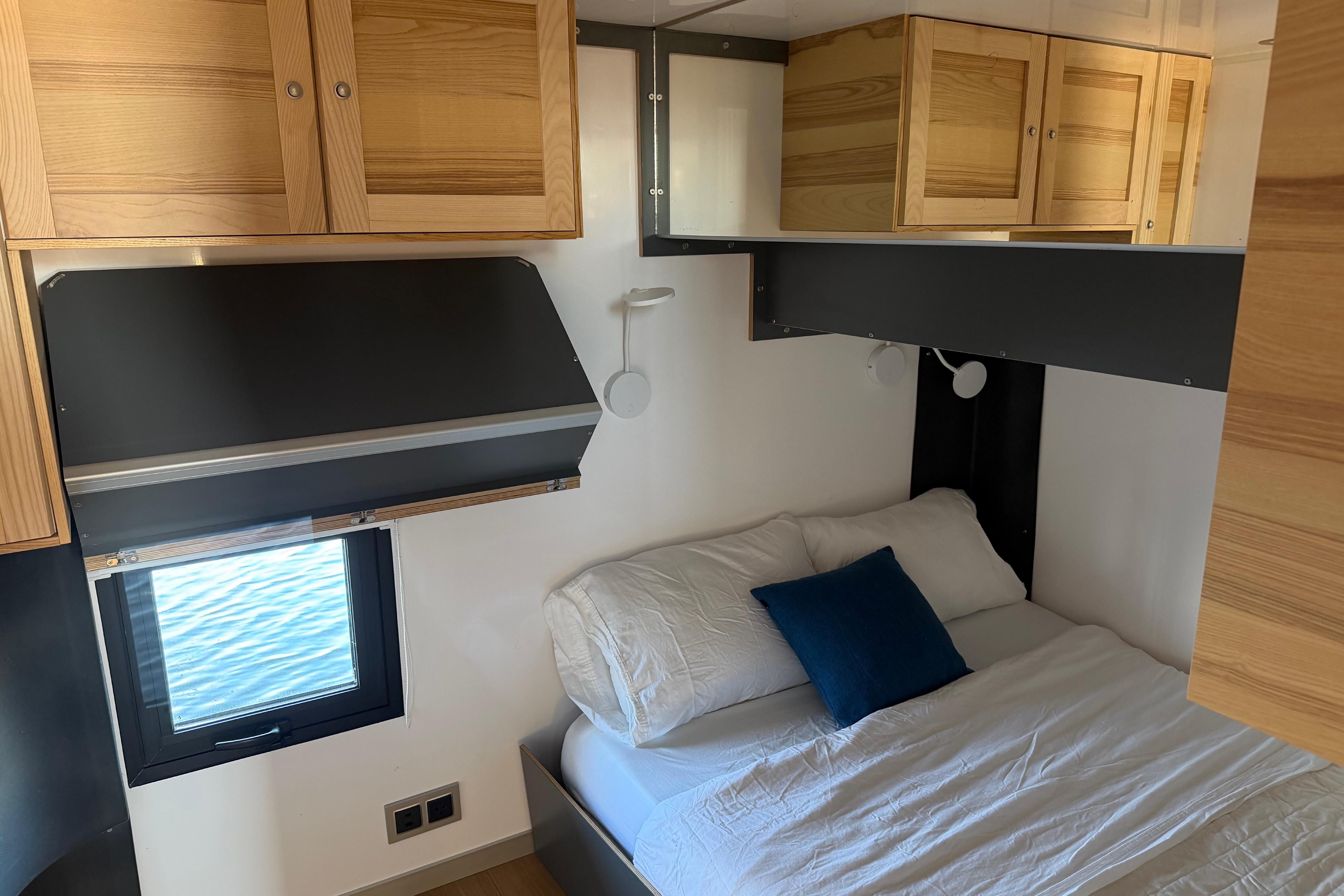 Cozy bedroom interior of 2022 Navisyo NV.08 with wooden cabinets and ocean view window.