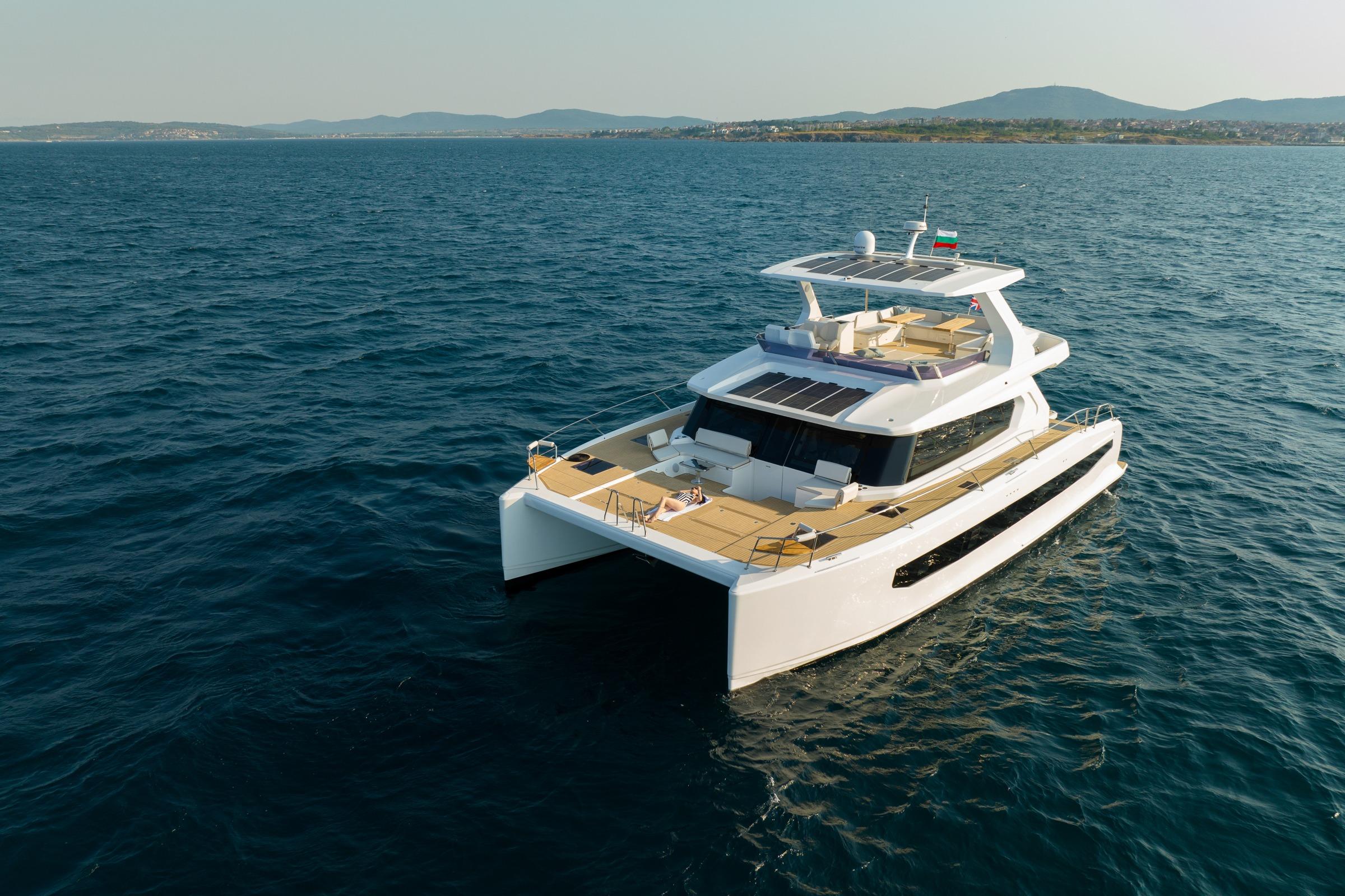 2025 Custom Omaya 50 Power Catamaran cruising on open sea with scenic coastline backdrop.