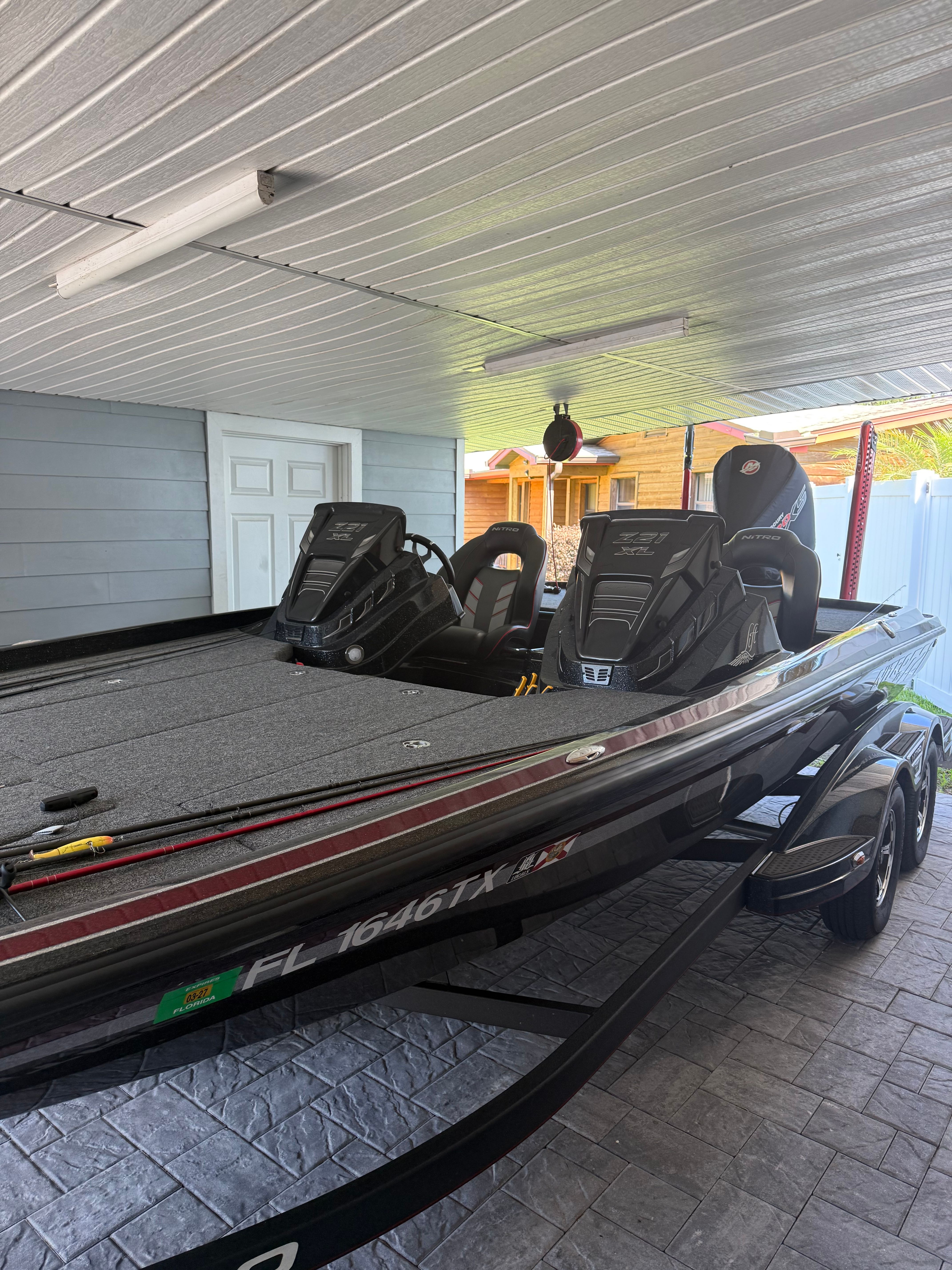 A modern fishing boat with two seats and a motor, parked under a covered area.