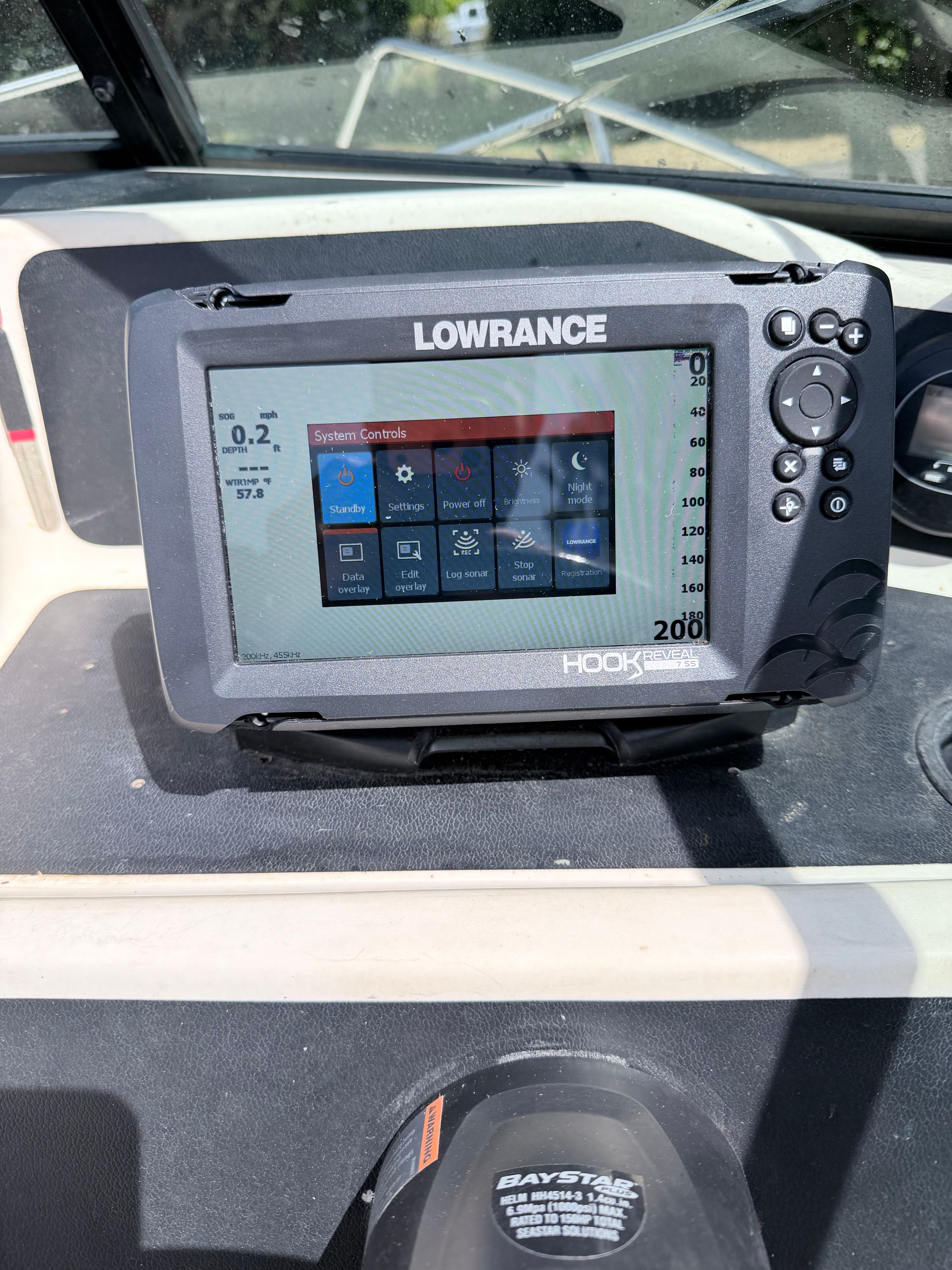 A Lowrance fish finder on a boat with control settings displayed on the screen.