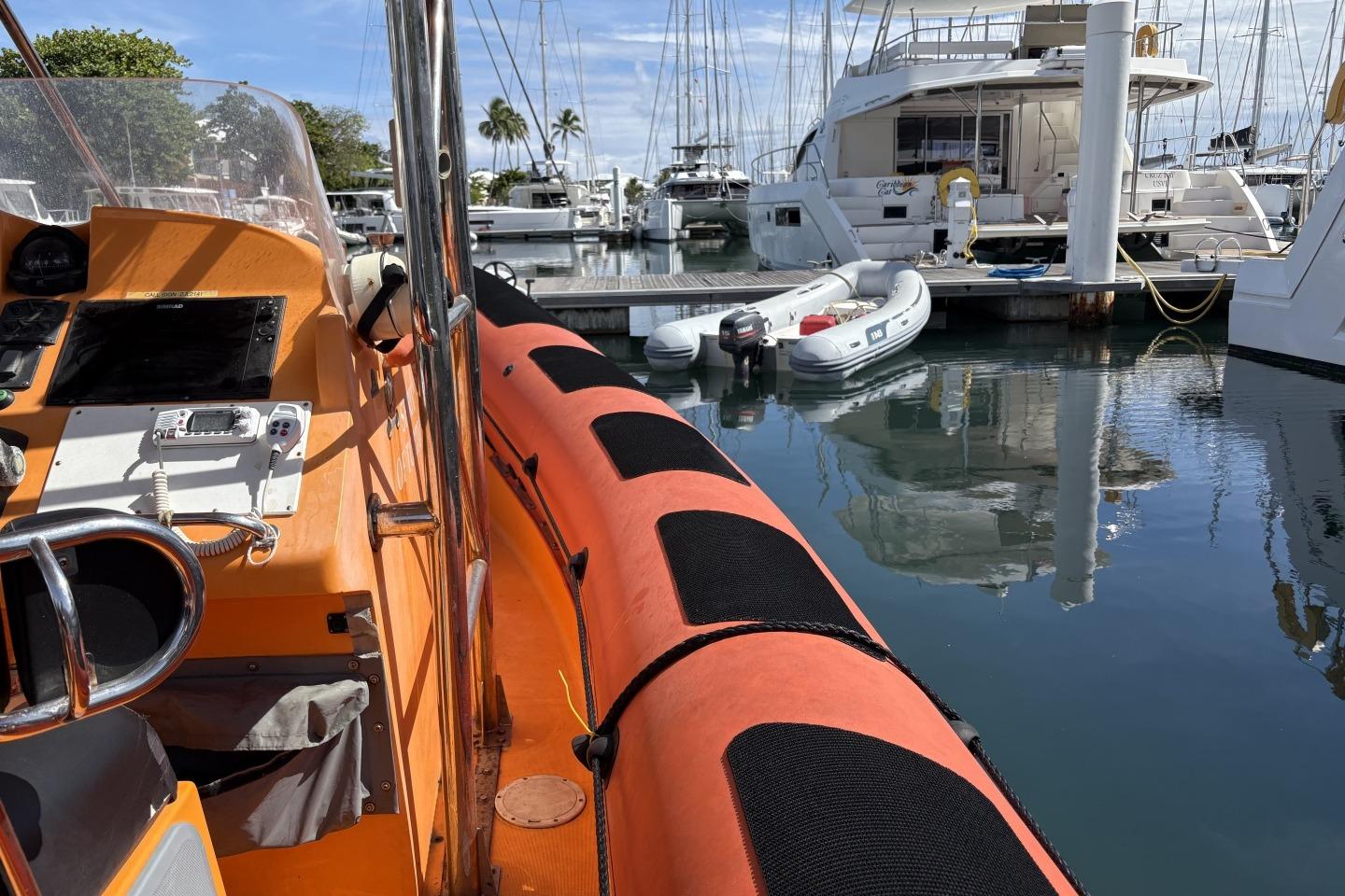 Orange Parker 1000 Baltic boat docked in marina, surrounded by yachts and clear water.