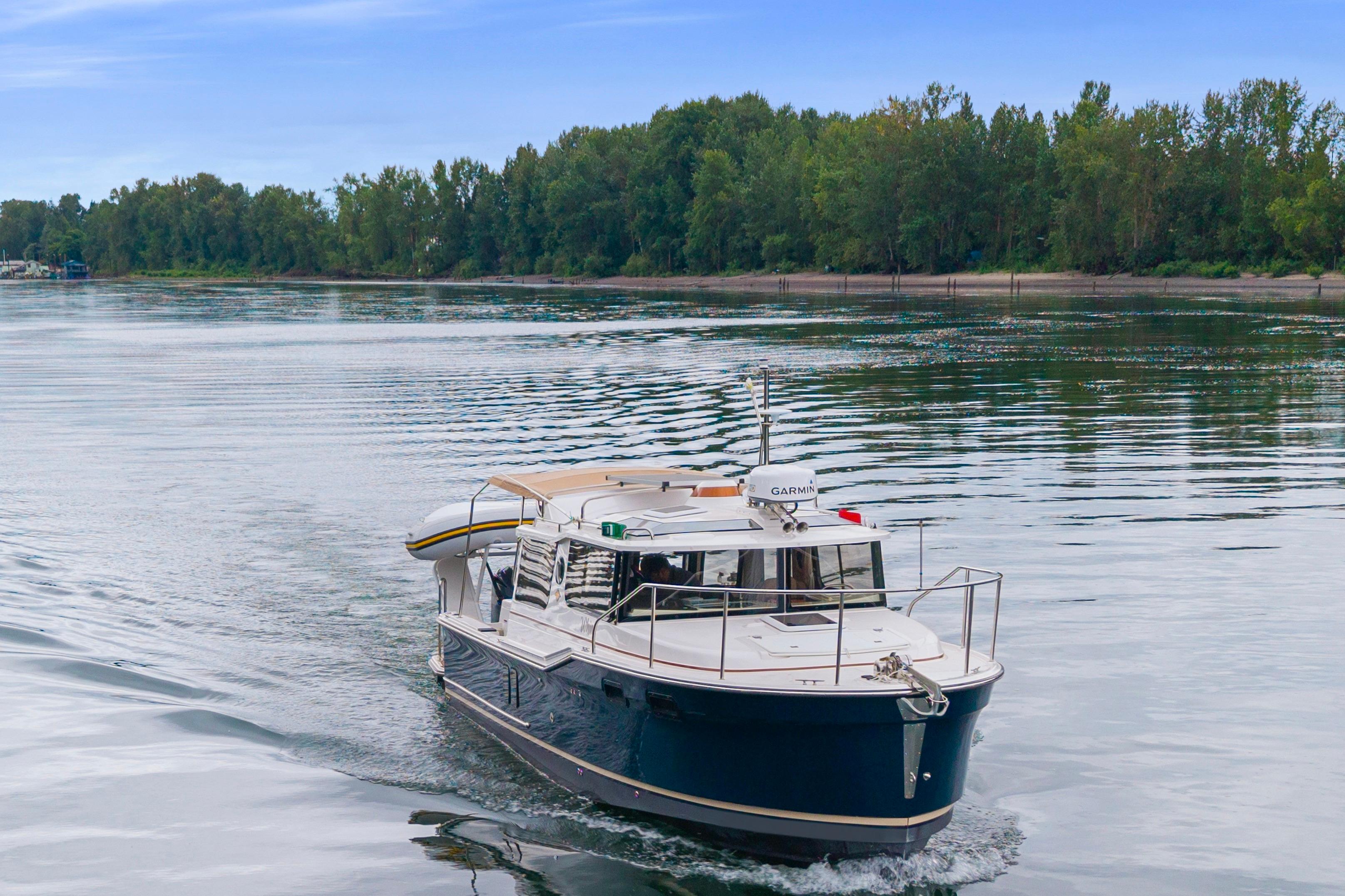 2022 Ranger Tugs R-27 cruising on a serene river with lush green trees.