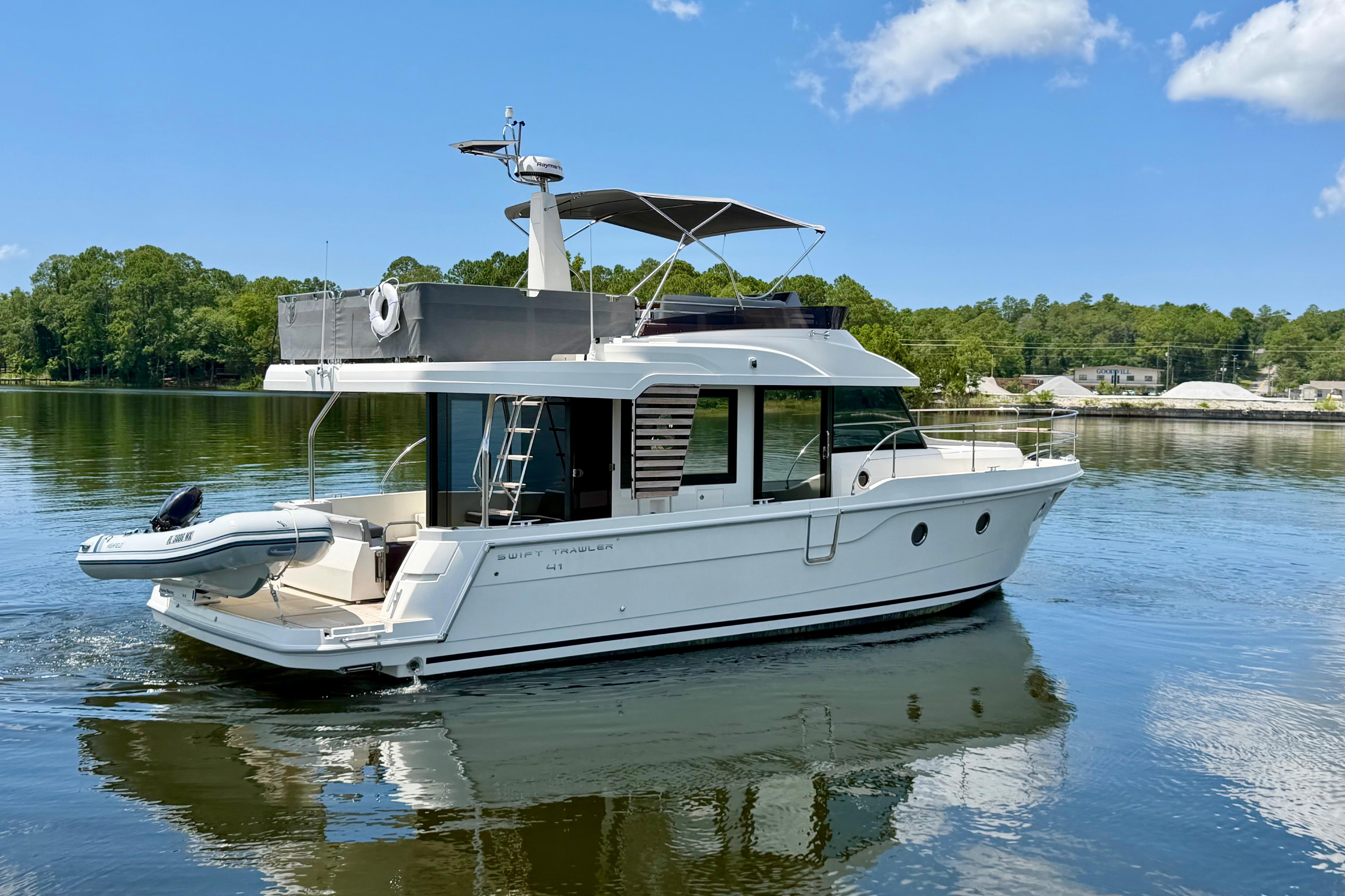 2025 Beneteau Swift Trawler 41 Fly cruising on a serene lake under a clear blue sky.