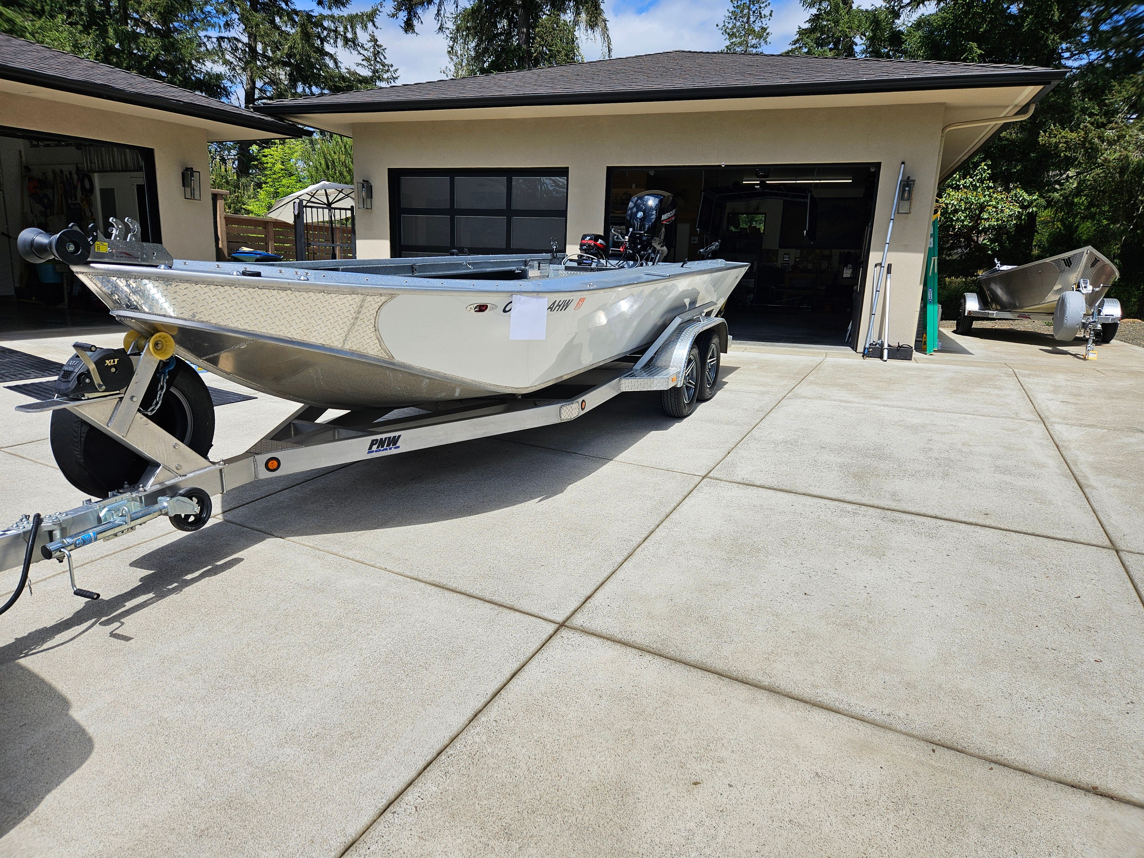 A silver boat on a trailer is parked in a driveway in front of a garage.