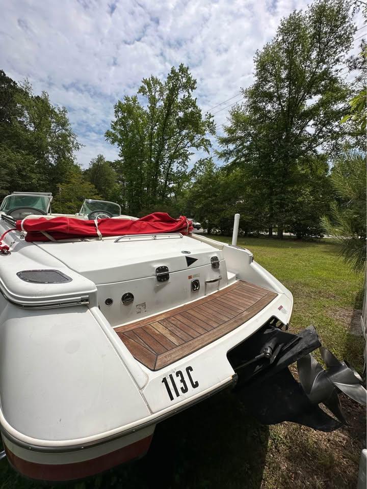 2001 Chris-Craft Launch 22 boat with red cover, parked on grassy area, surrounded by trees.