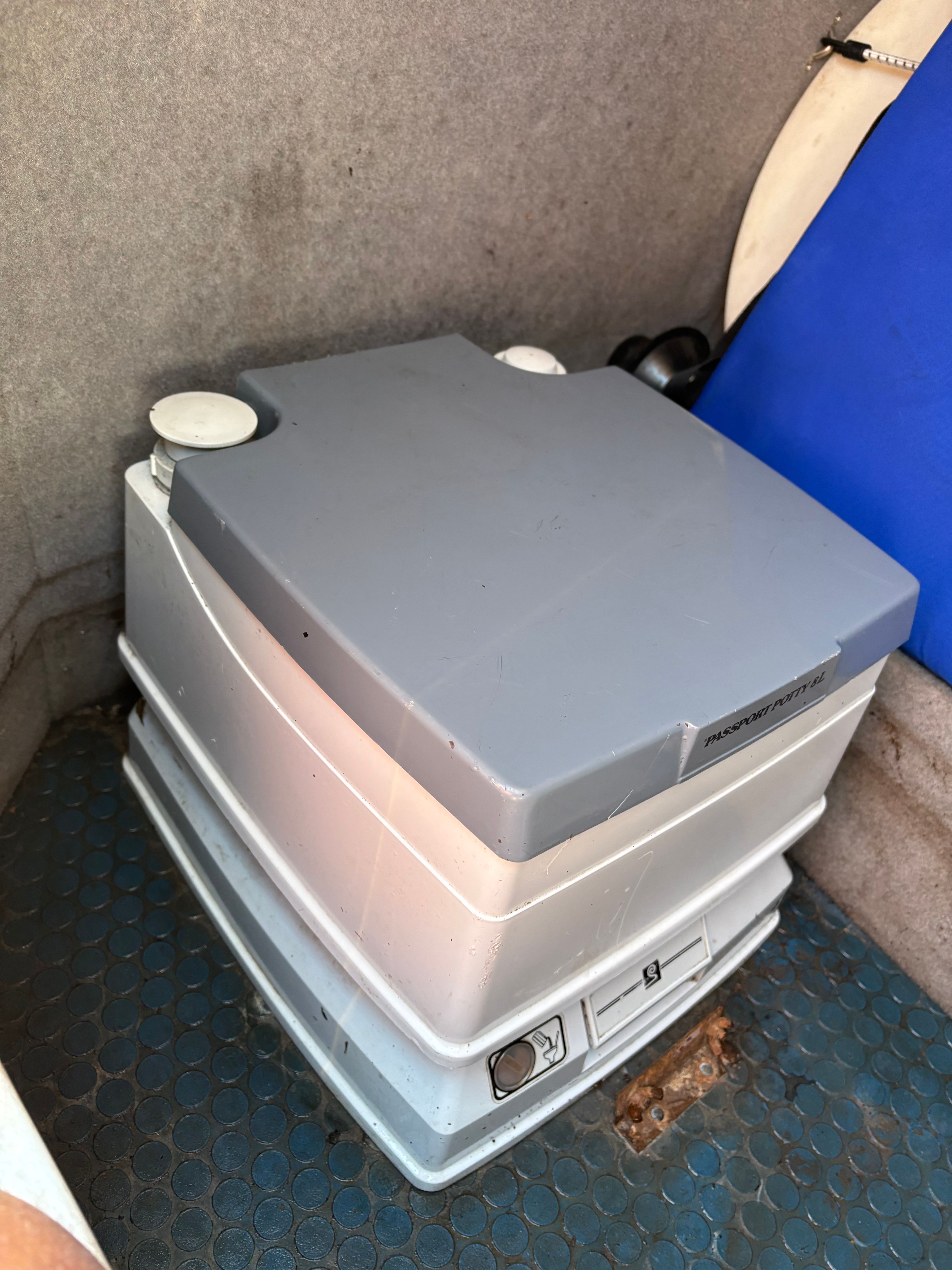 Portable toilet in a boat with a gray lid and blue upholstery.