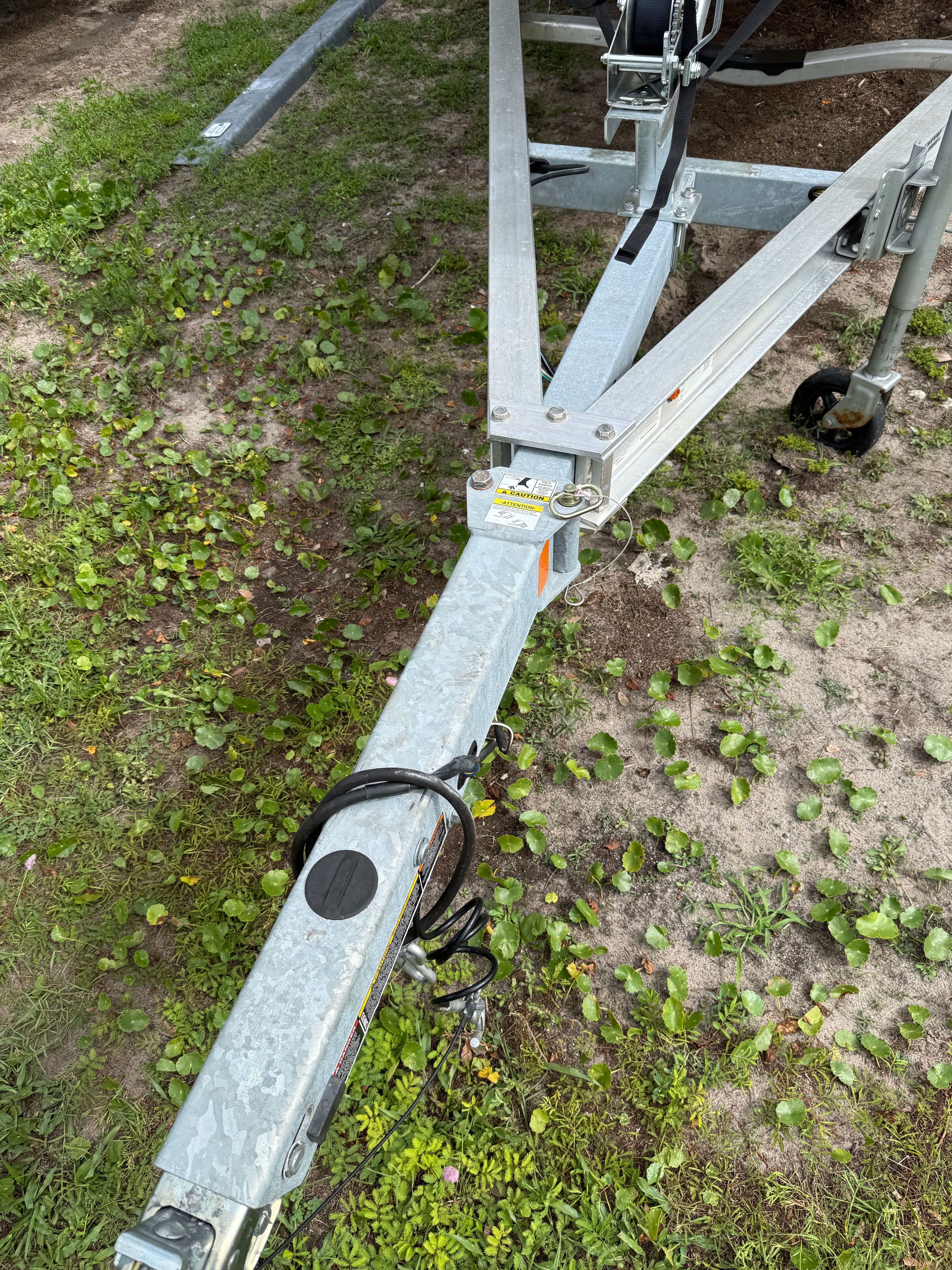 A boat trailer on grassy ground, featuring a metal frame and hitch.