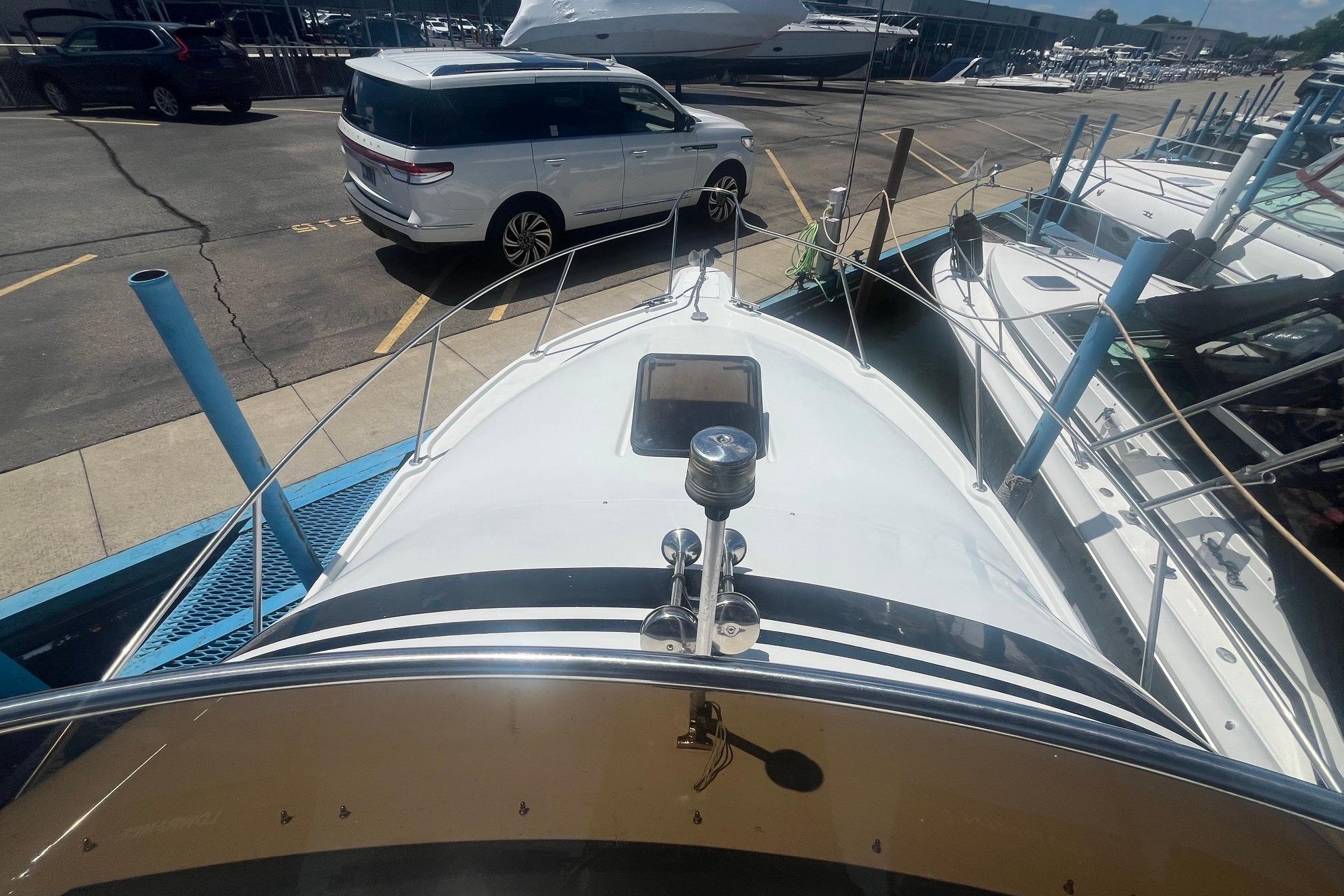1988 Seafox 29 Flybridge boat docked, viewed from the bow, with nearby parked vehicles.
