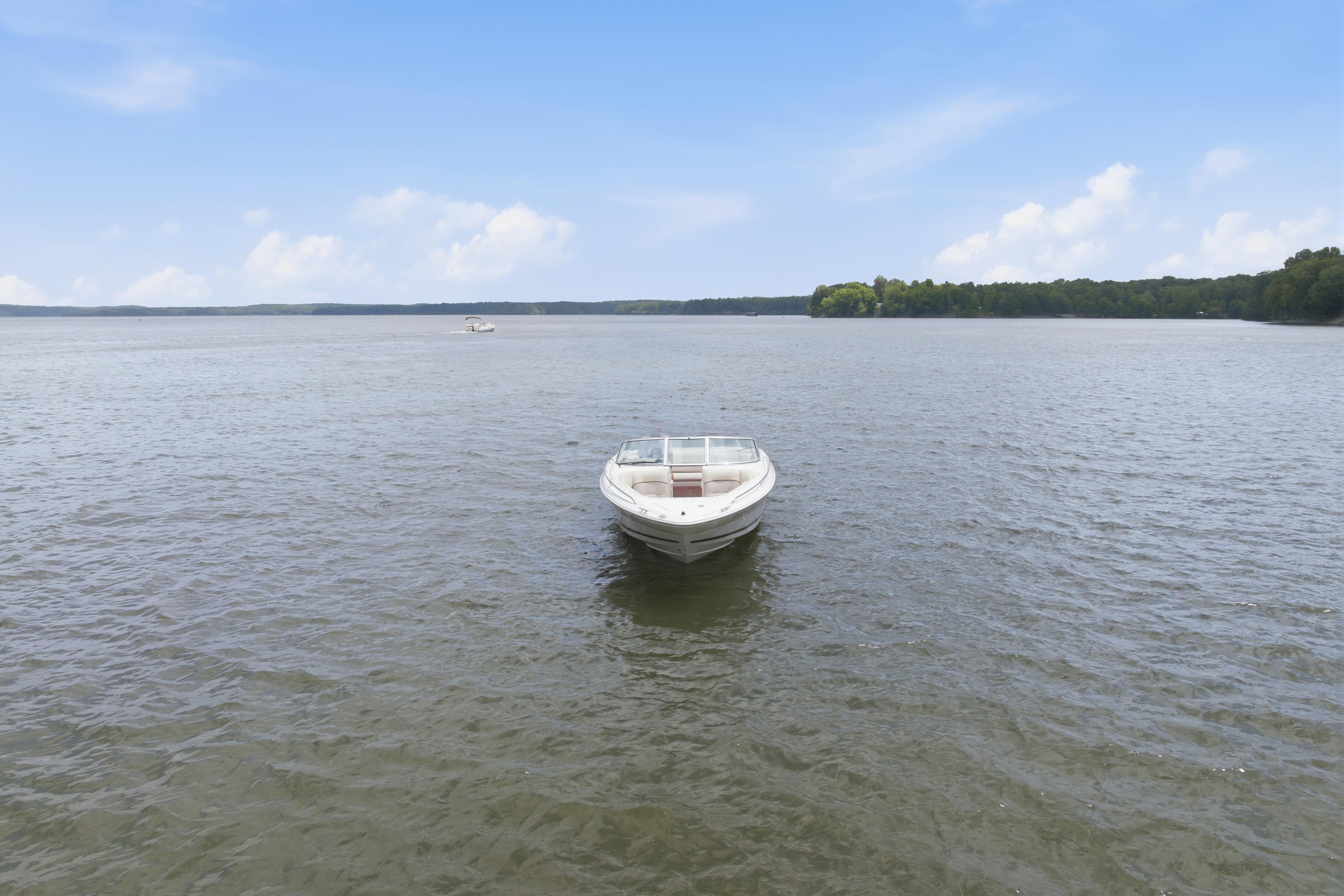 1997 Sea Ray 230 Signature boat on calm lake under clear blue sky.