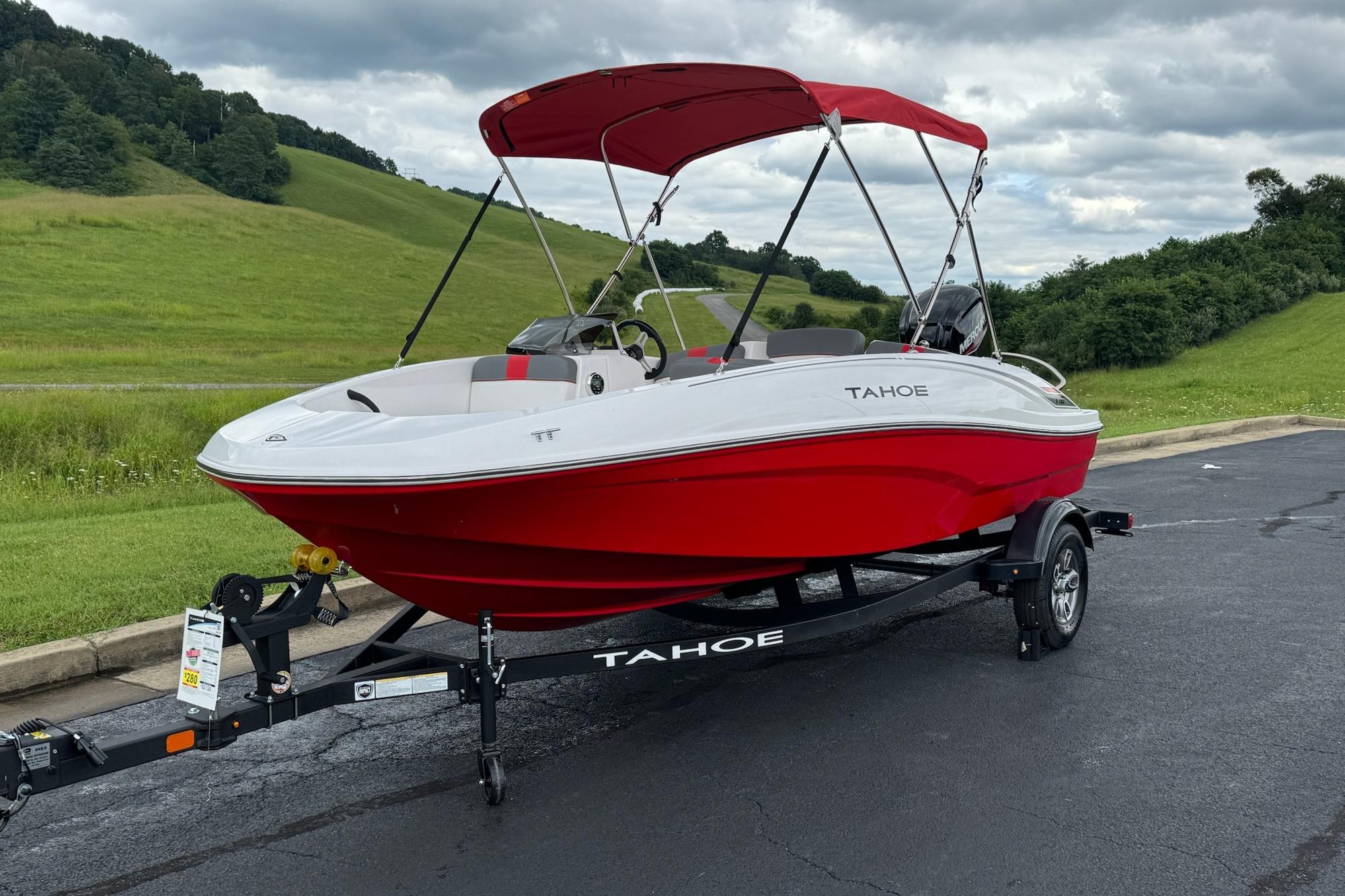 2026 Tahoe T16 boat with red hull on trailer, parked on asphalt near grassy hills.
