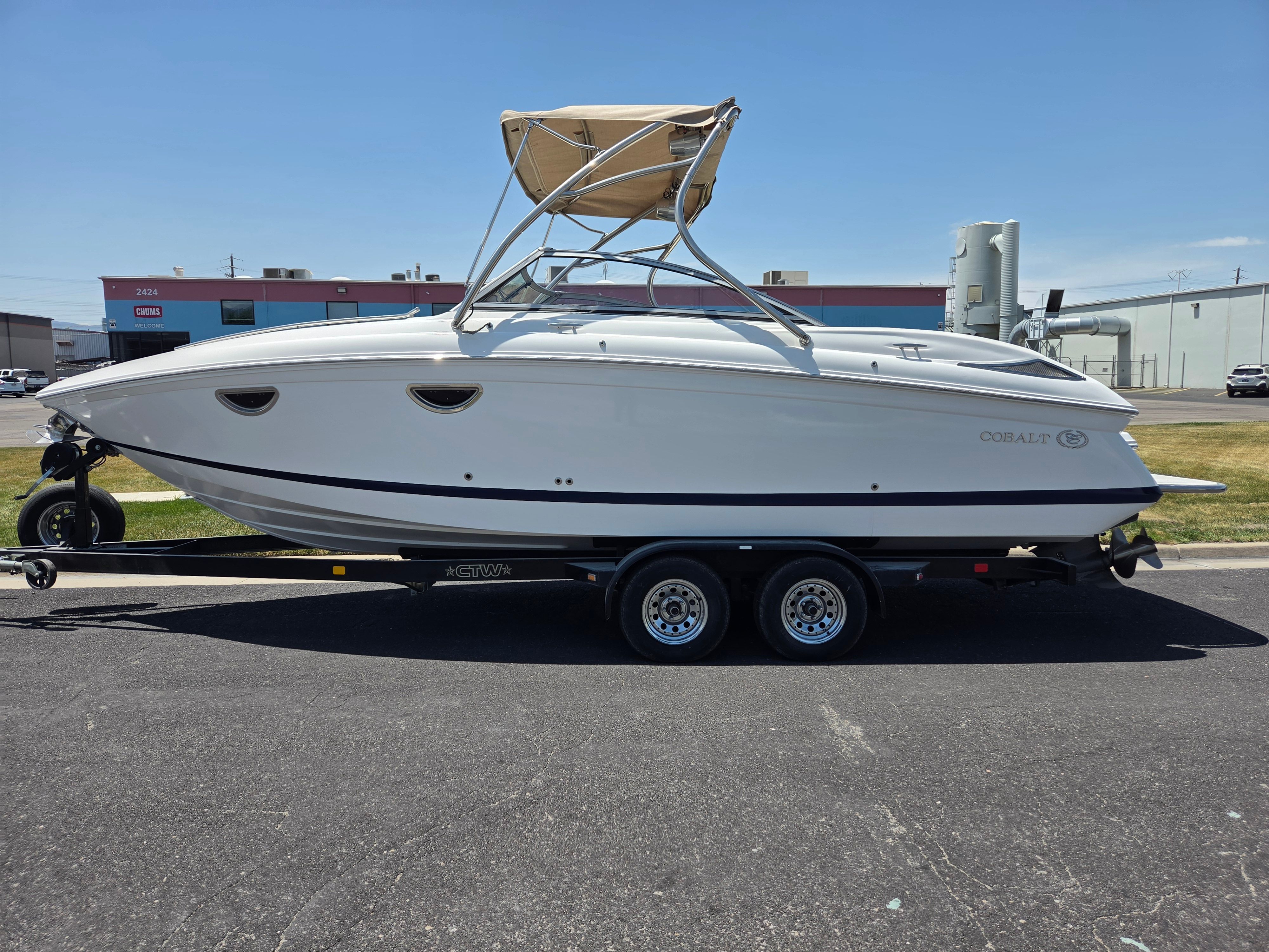 A white Cobalt 243 boat on a trailer, parked in a lot.
