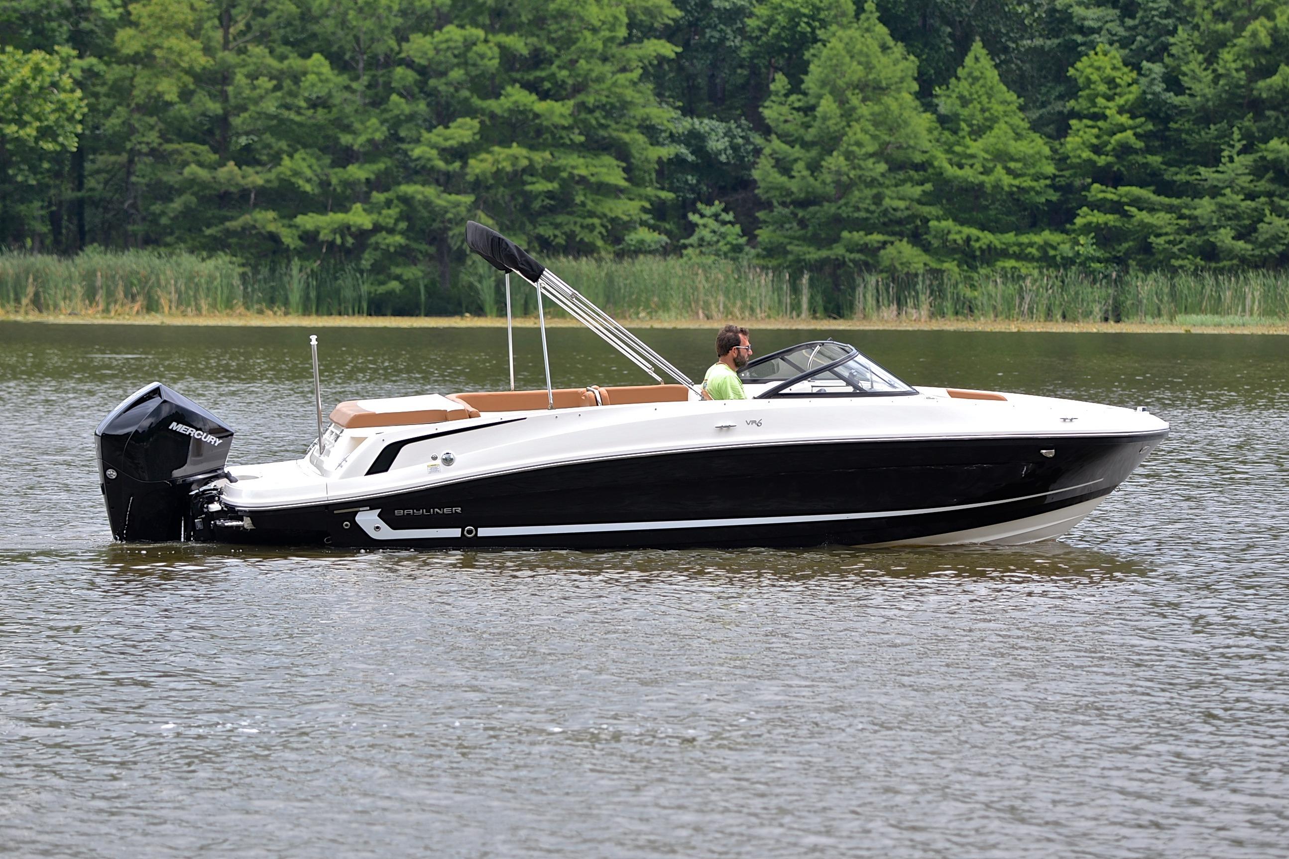 2019 Bayliner VR6 Bowrider OB cruising on a calm lake with lush green trees.