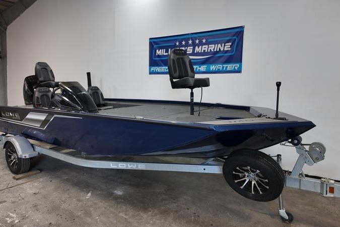 2024 Lowe Stinger 198 boat on trailer in showroom, blue exterior, banner in background.