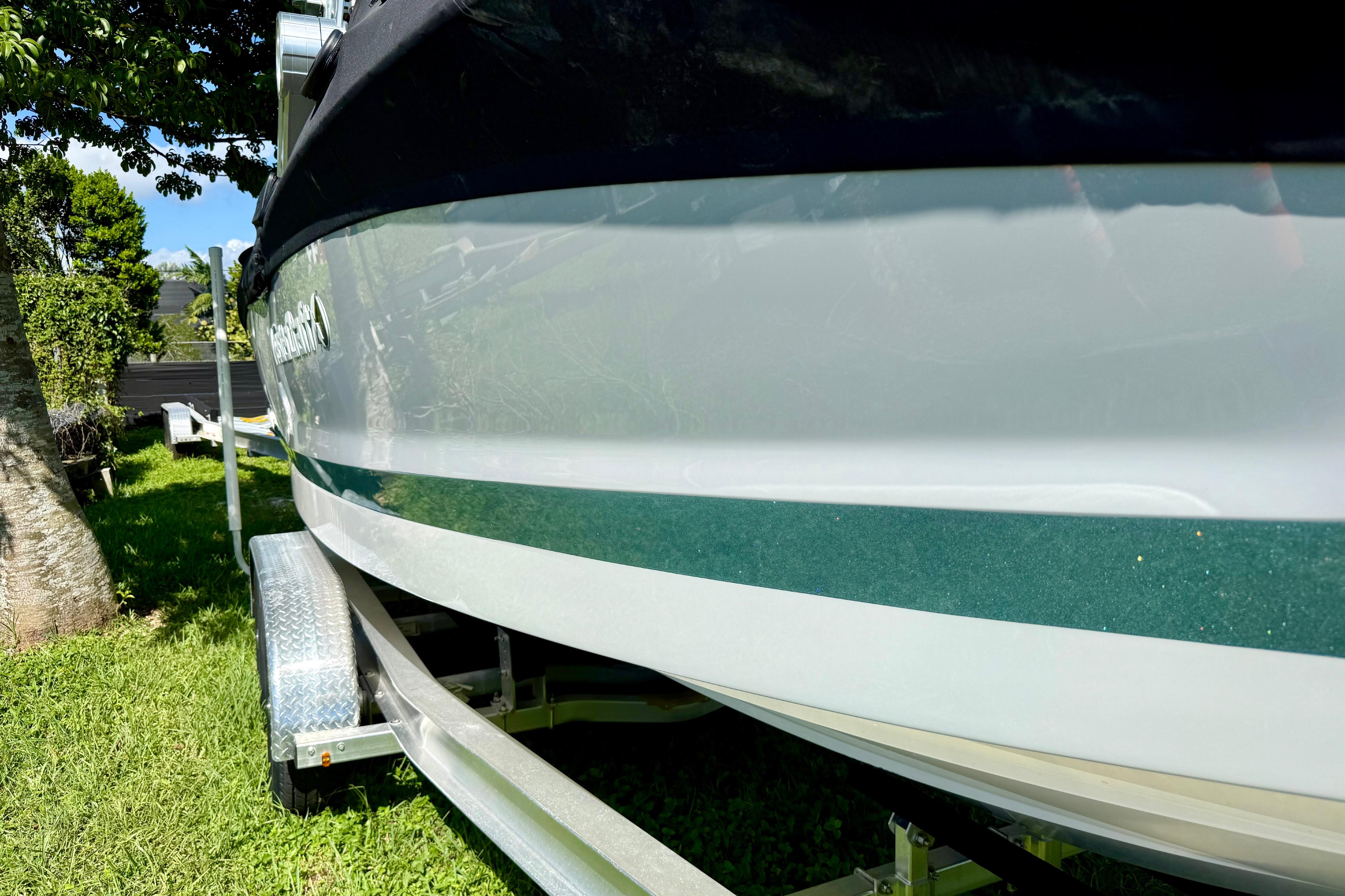 2023 MasterCraft X24 boat on trailer, parked on grass under a tree.