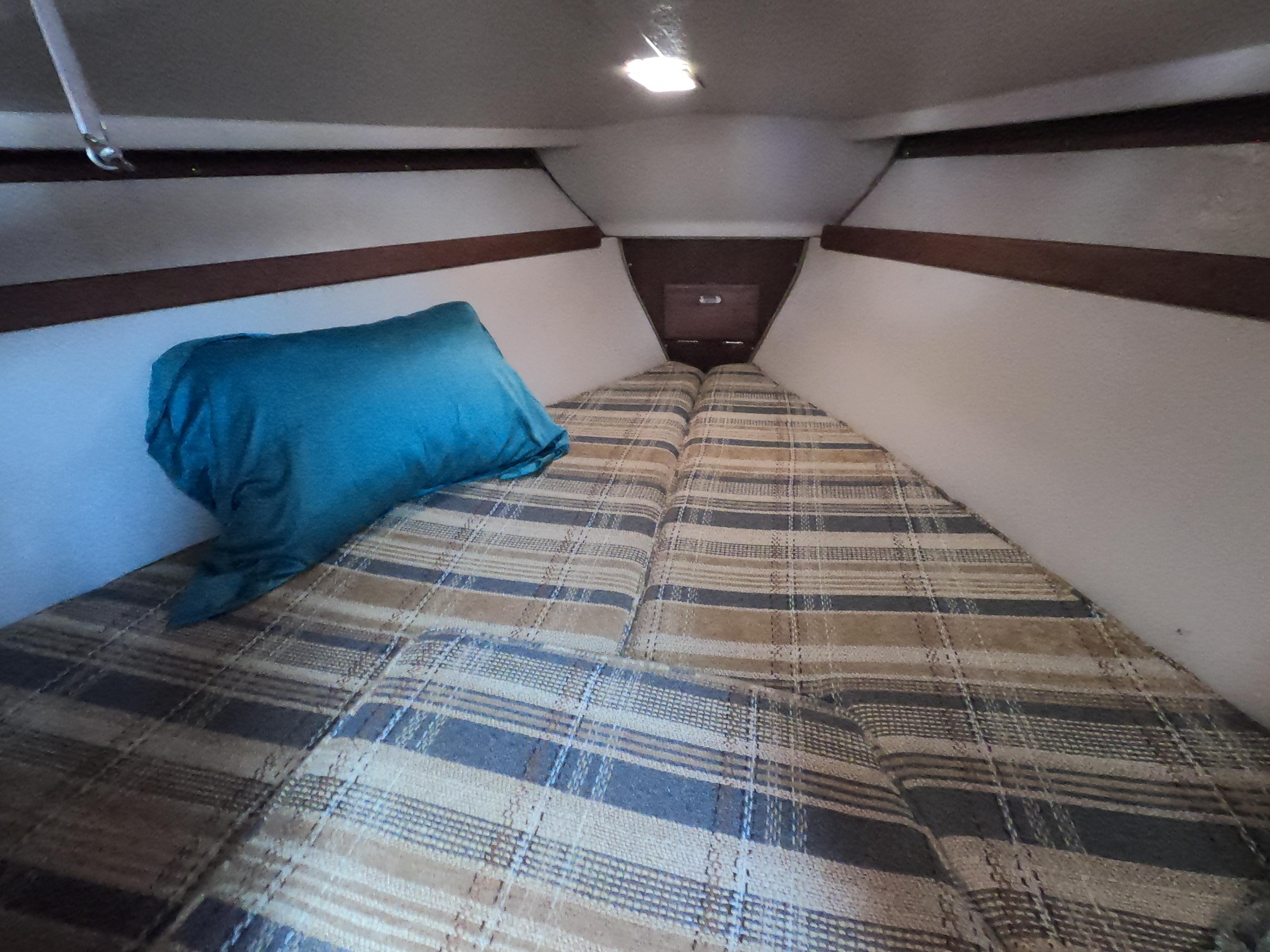 Cozy cabin interior of a 1985 Catalina 30 sailboat with plaid bedding and a blue pillow.