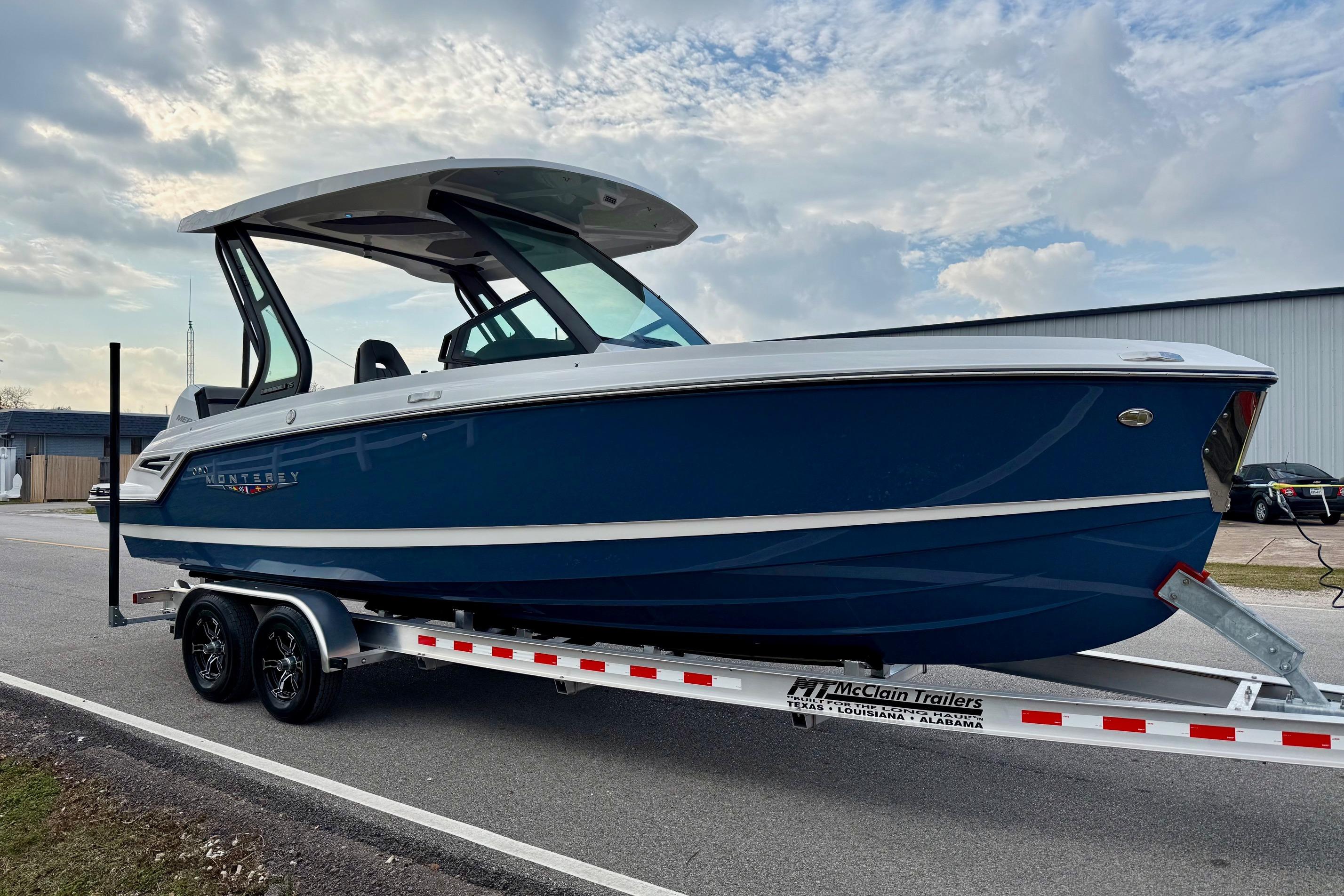 2026 Monterey Elite 25 OB boat on trailer, blue hull, parked outdoors.