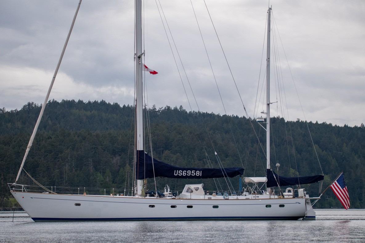 Sailing yacht Abeking & Rasmussen Tripp 74, 1968, on calm water with forested background.