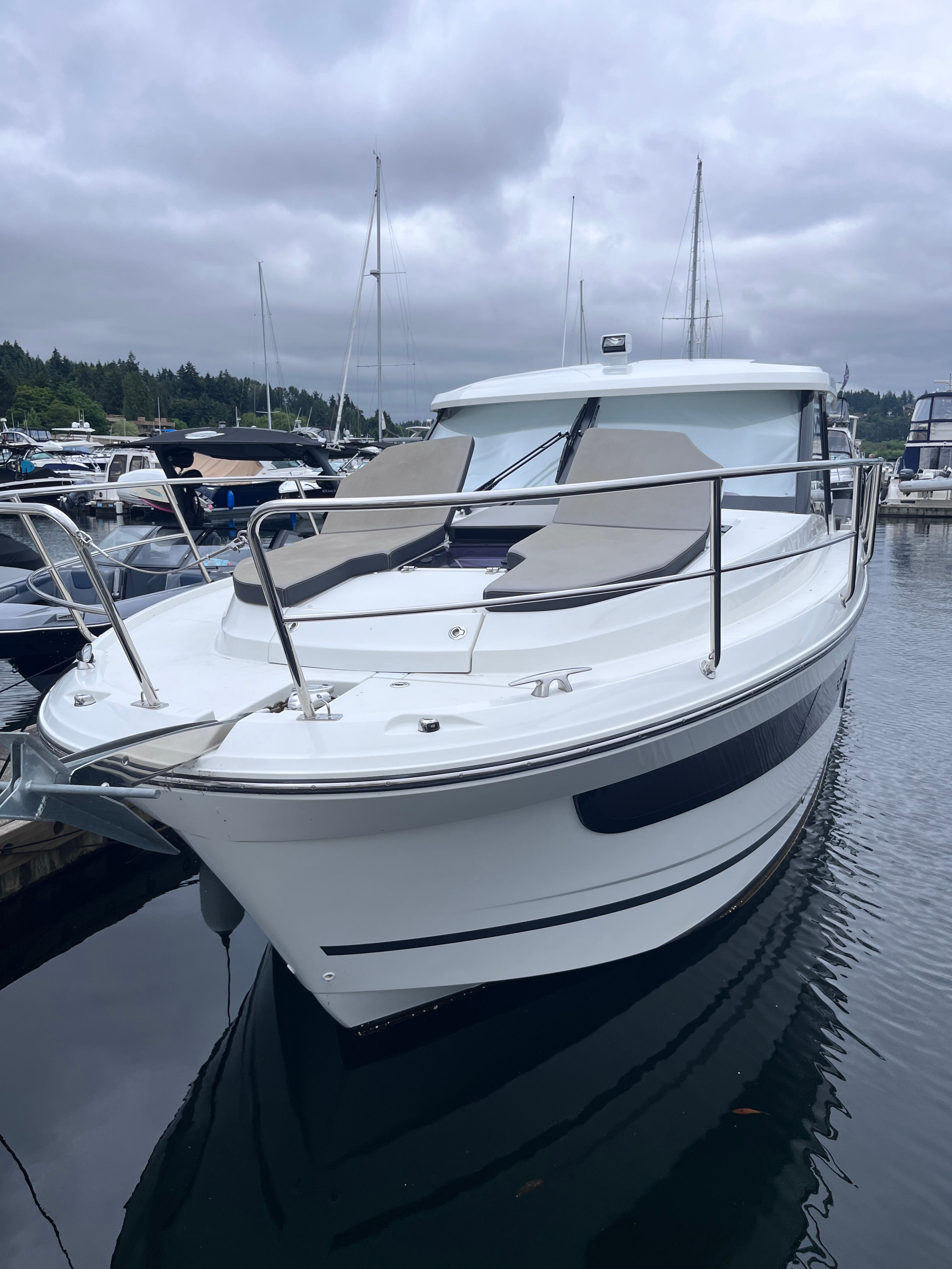 A 2021 Jeanneau NC 1095 boat docked in a marina. It features a sleek design and comfortable sun pads.
