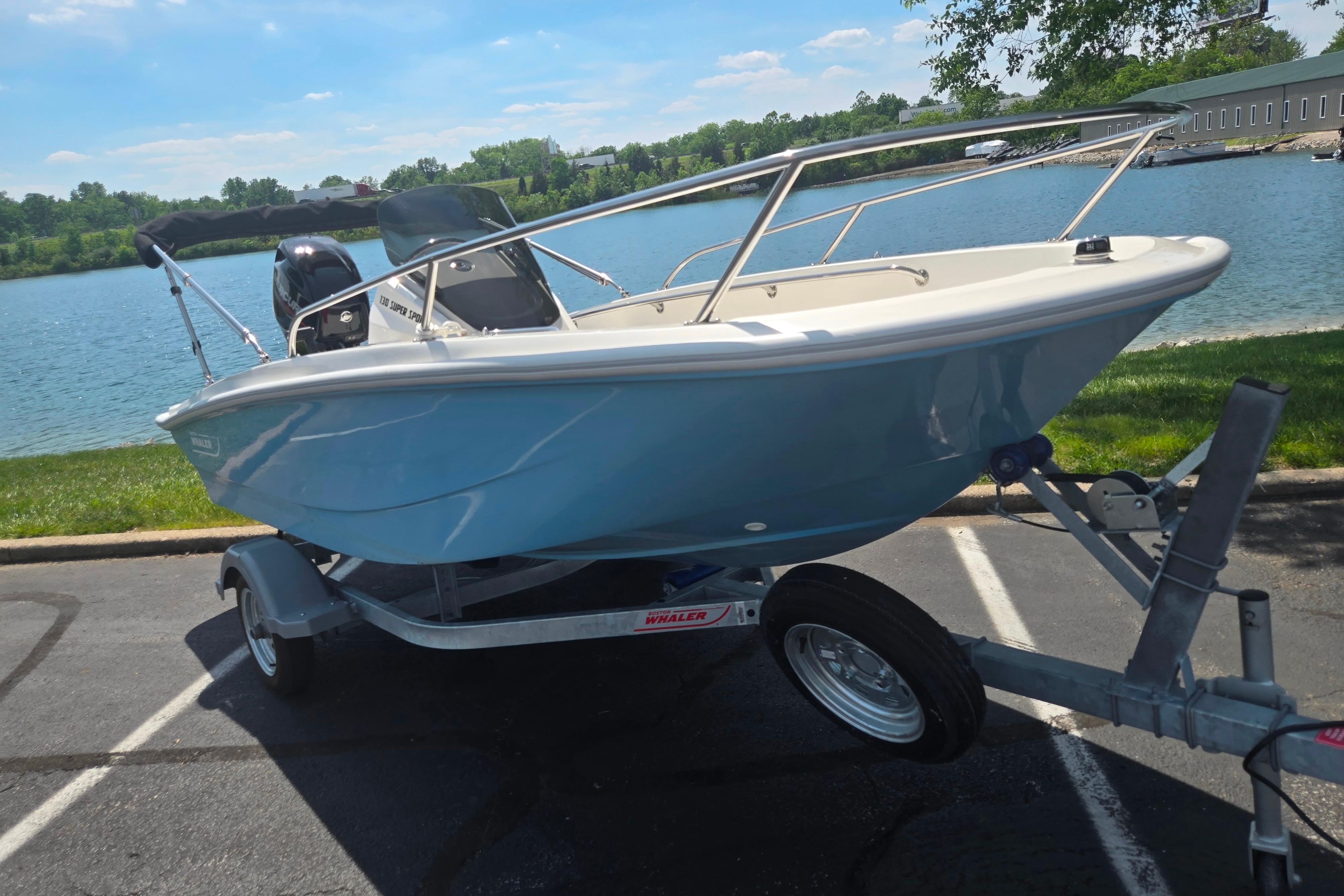 2025 Boston Whaler 130 Super Sport boat on trailer by a scenic lake.