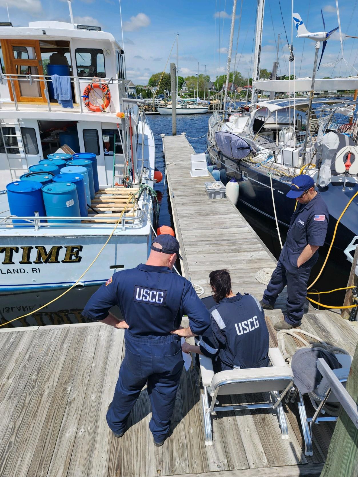 USCG officers inspecting docked boats, including a 1980 Tuna Rose Brothers model, on a sunny day.