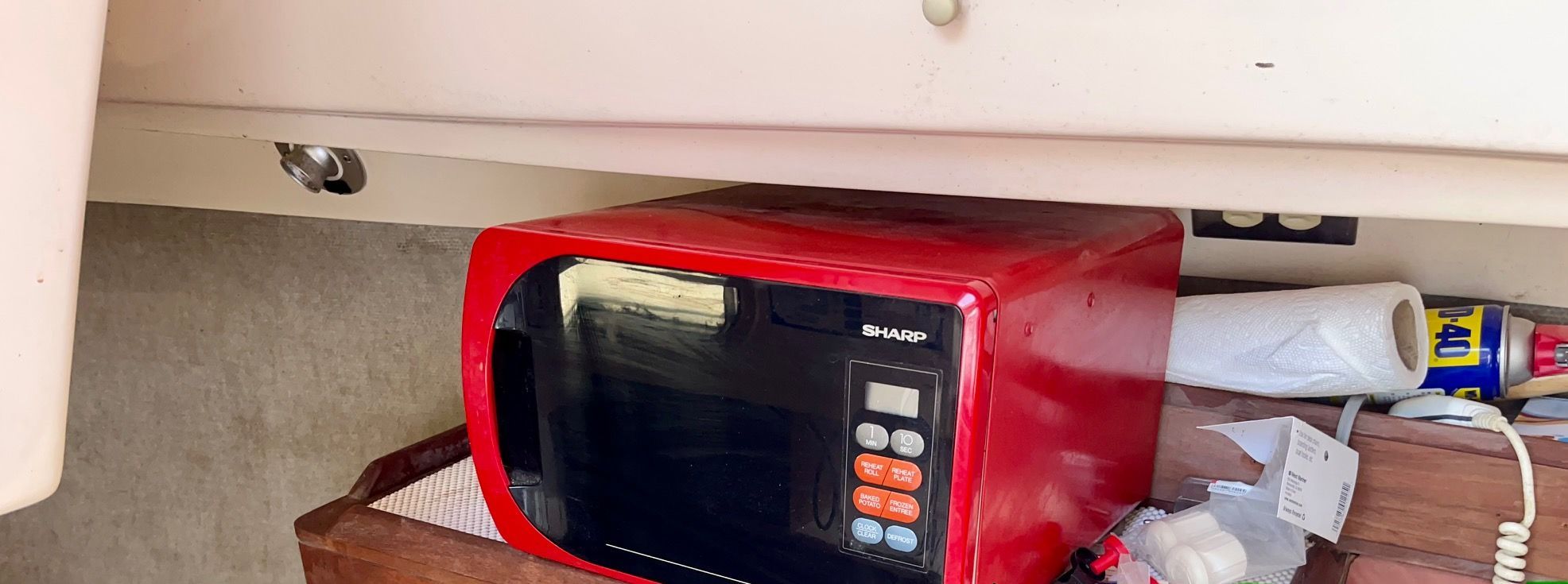 Red microwave in a boat galley with wooden countertop and storage space.