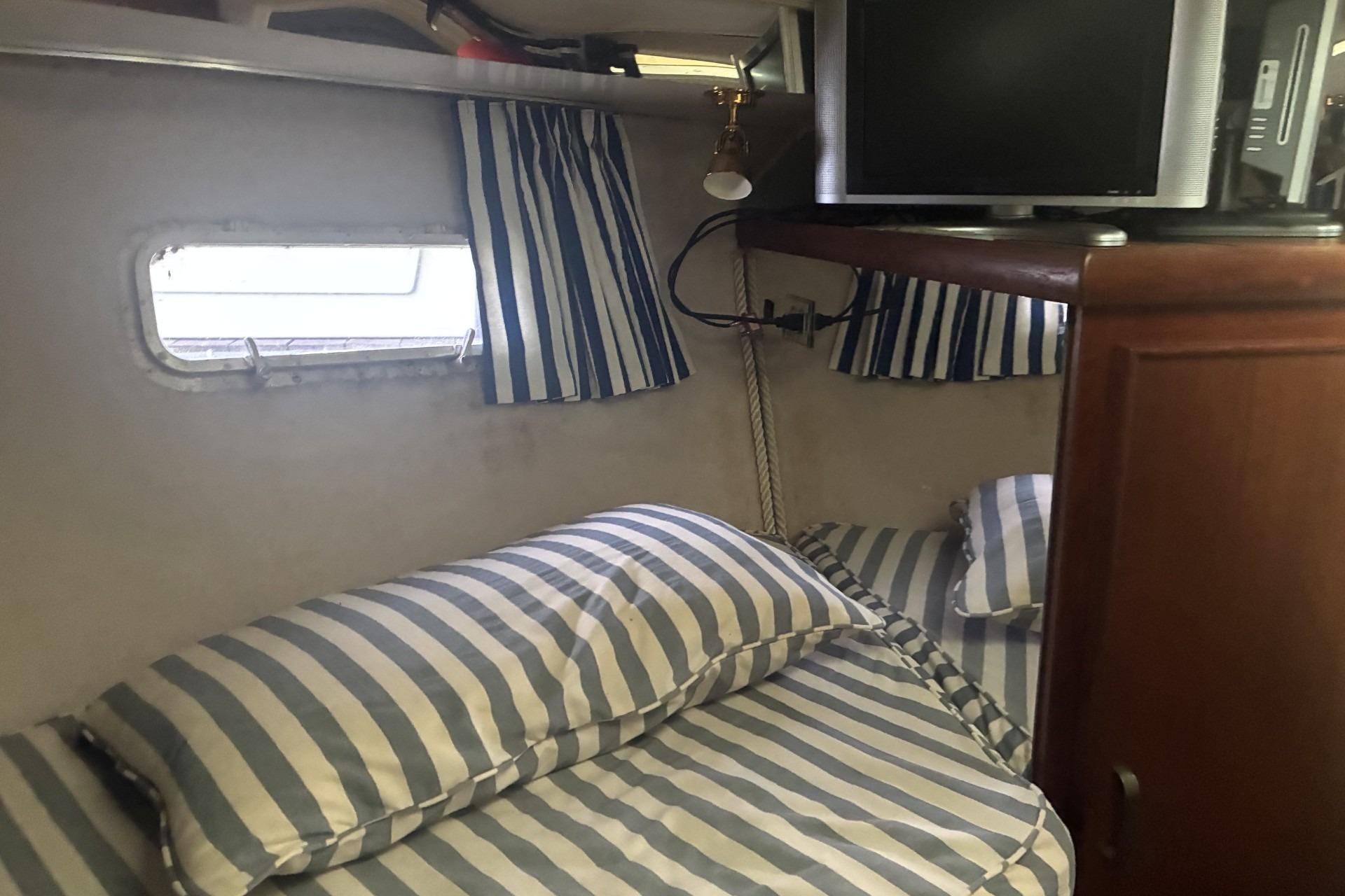 Interior cabin of 1980 Chris-Craft 360 Commander with striped bedding and a small TV.