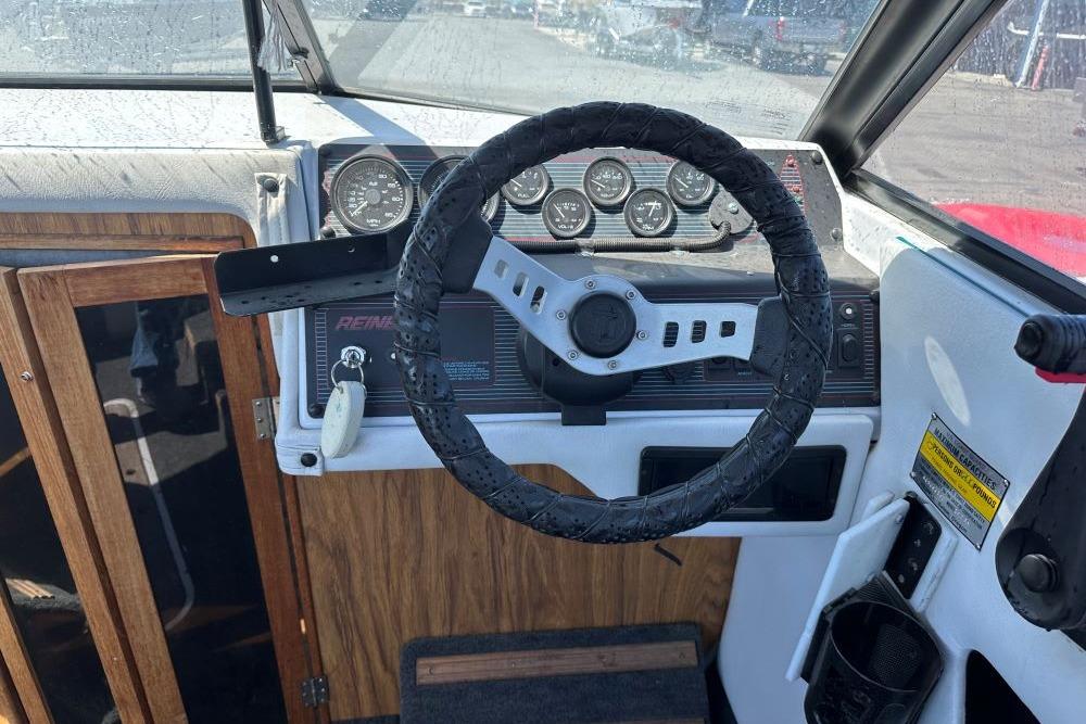 Steering wheel and dashboard of a 1992 Reinell 192 RM boat, featuring gauges and wood accents.