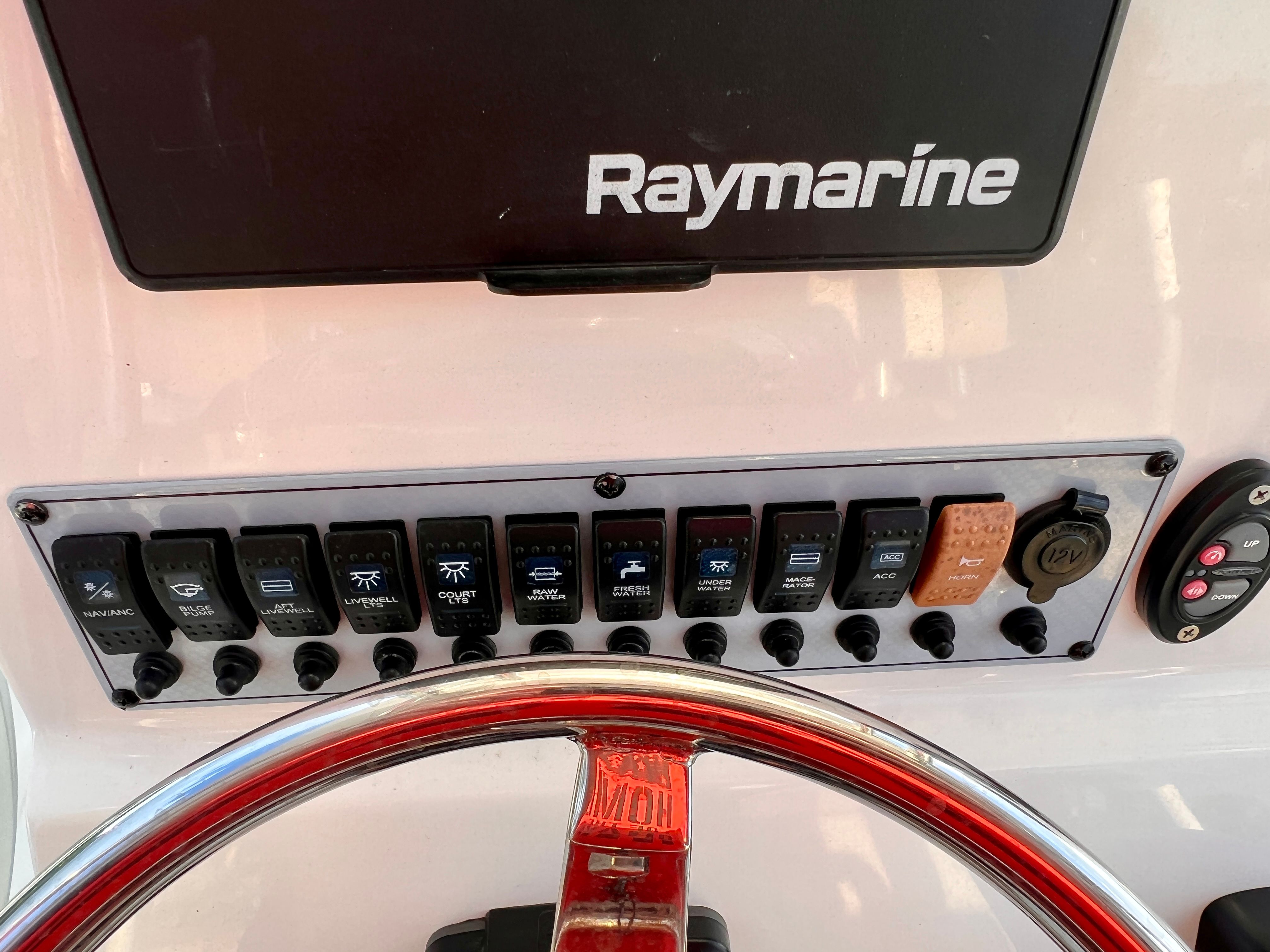 The image shows a boat dashboard with a Raymarine display and multiple switches.