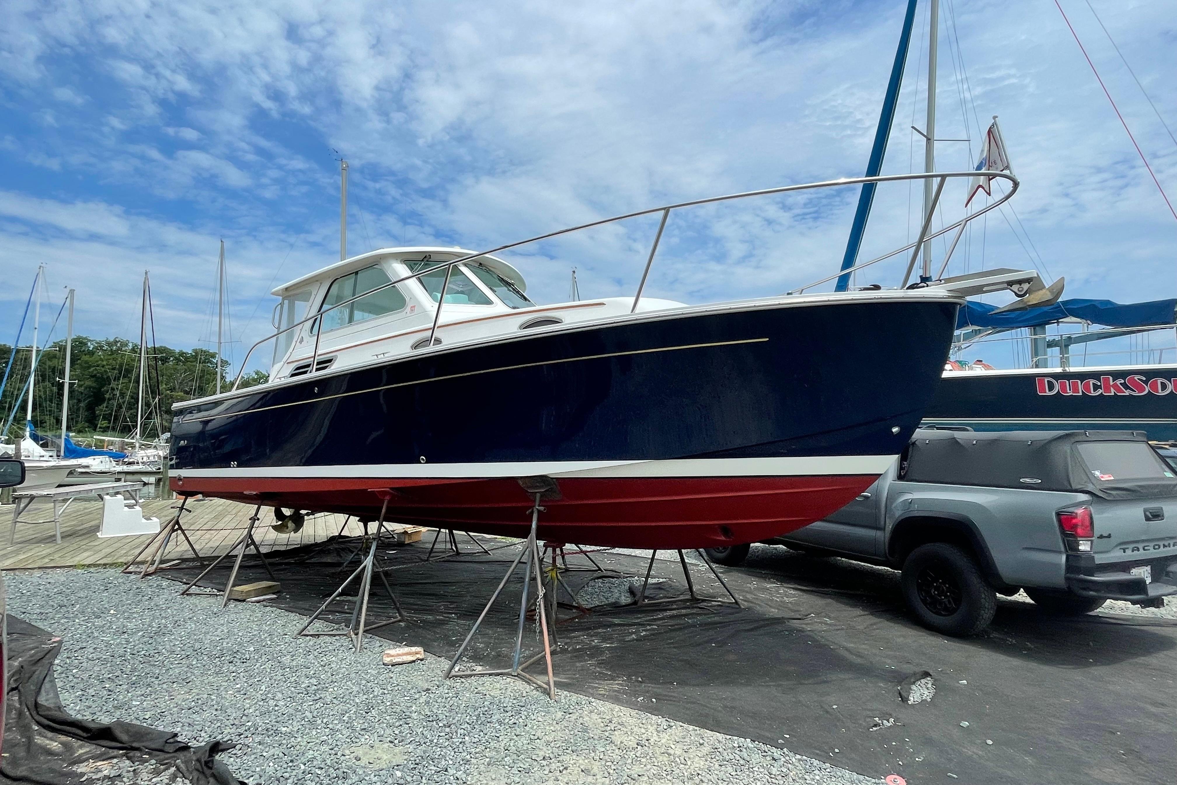 2007 Back Cove 29 boat on stands, blue hull, red bottom, marina background.