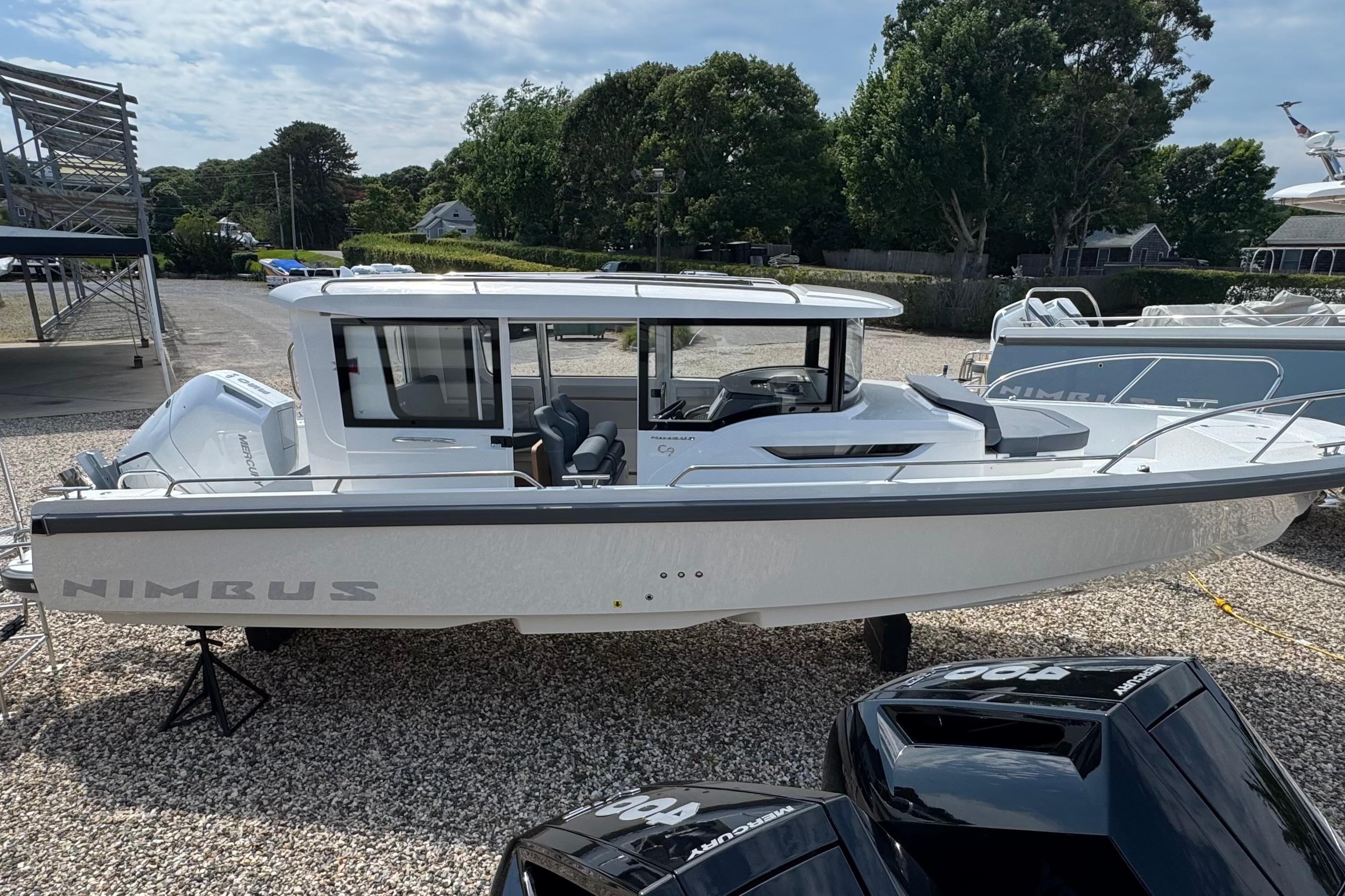 Nimbus Commuter 9 from 2026 on a gravel lot, surrounded by trees and other boats.