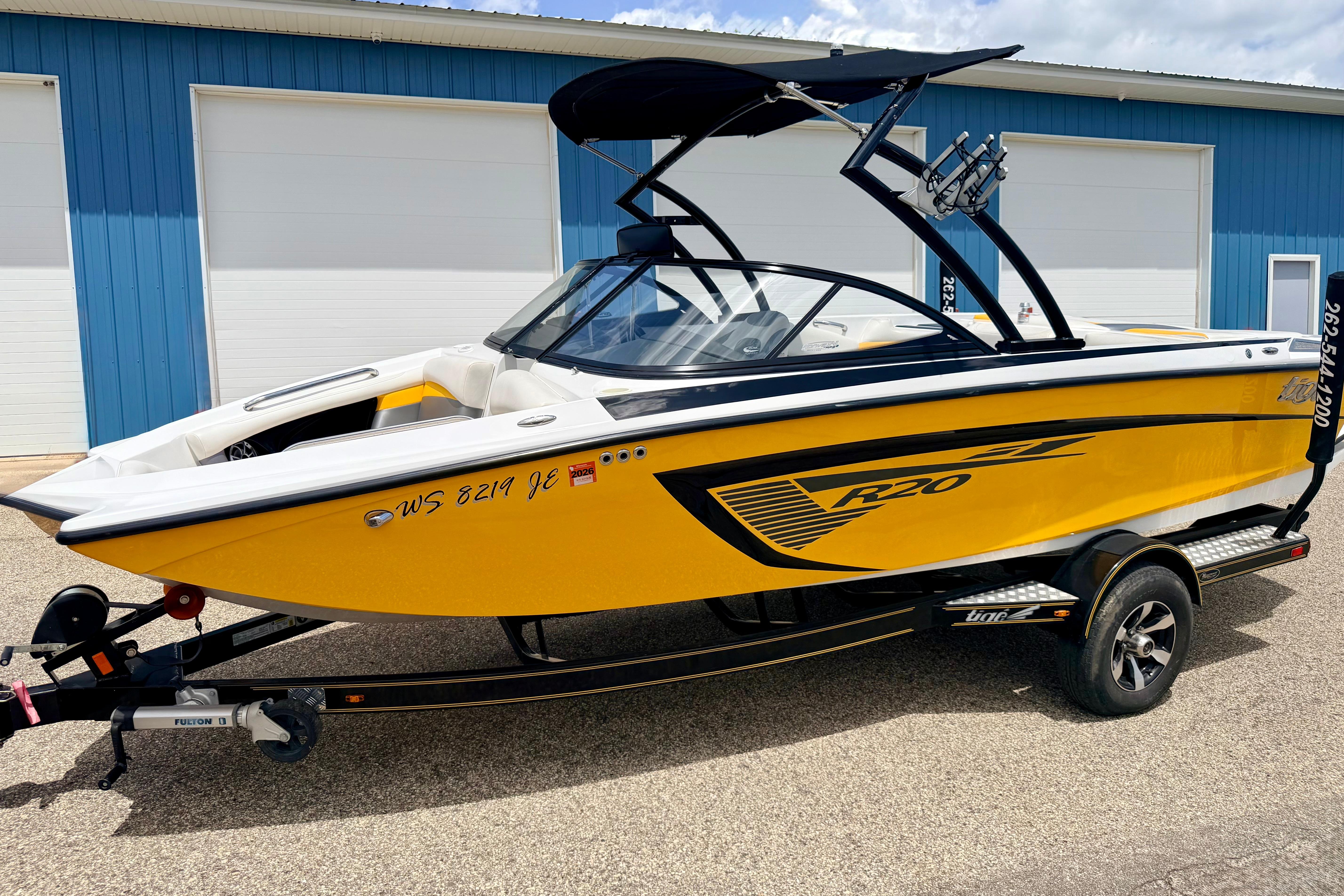 2014 Tigé R20 yellow boat on trailer, parked near blue building.