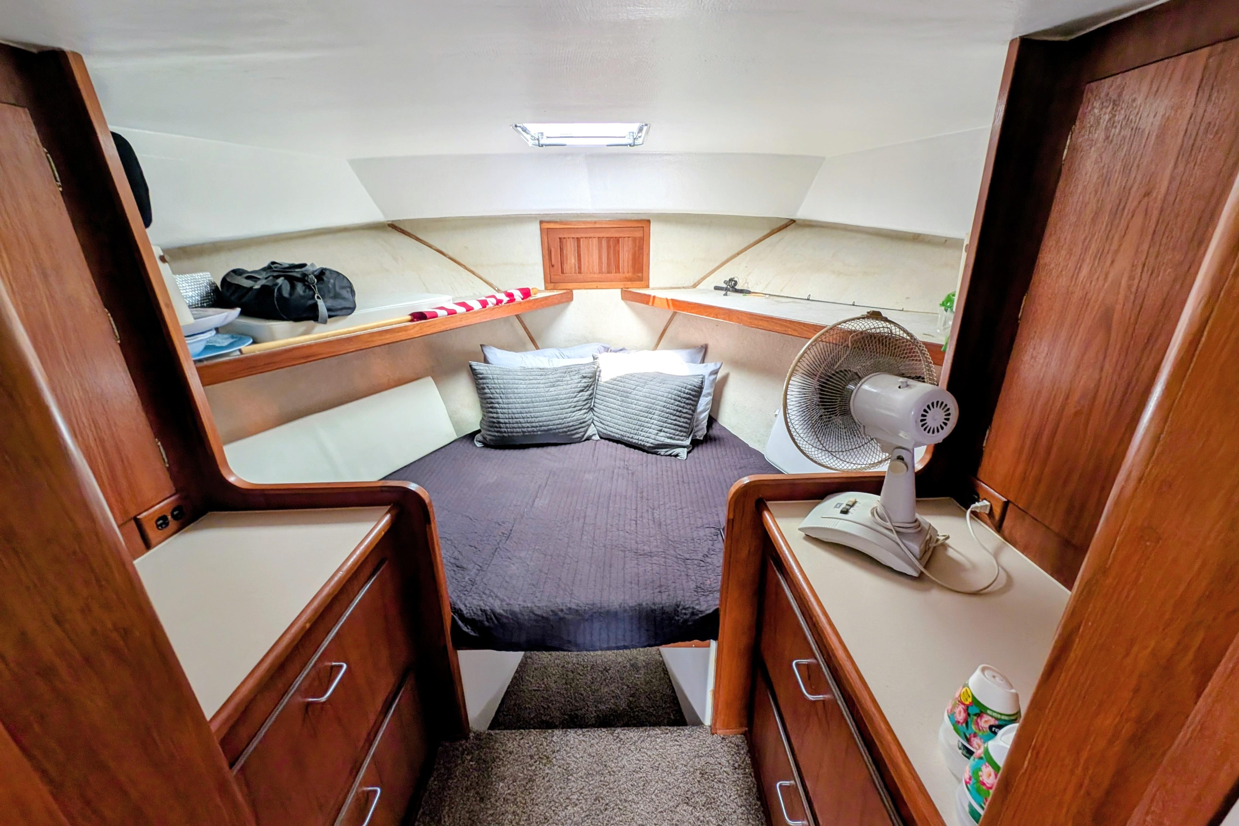 Cozy cabin interior of 1998 Markley 46 boat with bed, fan, and wooden cabinetry.
