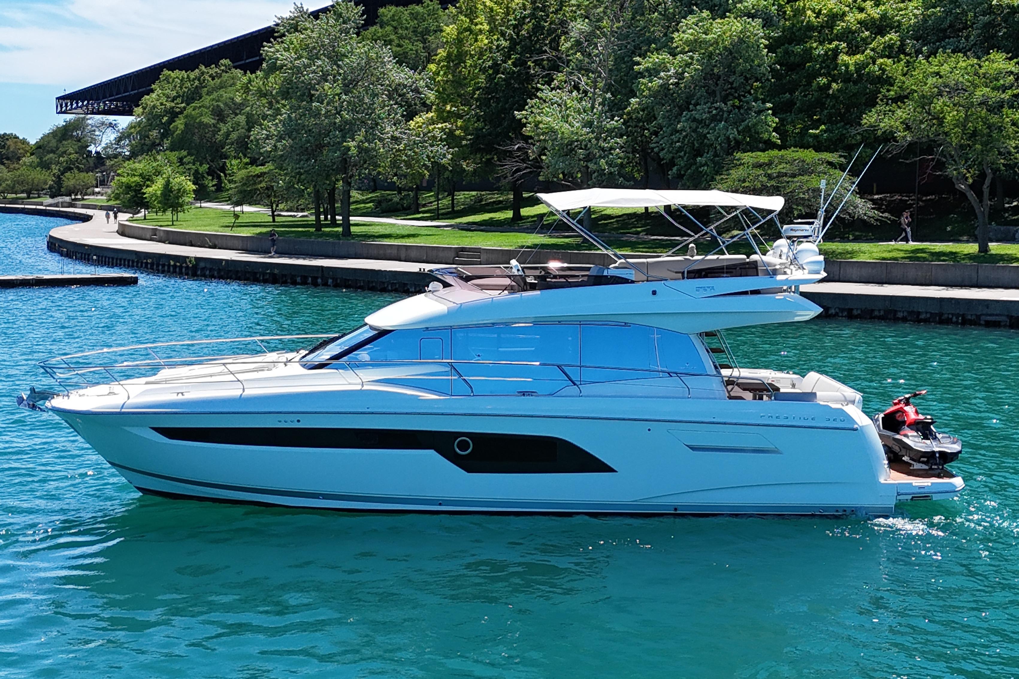 Luxury 2022 Prestige 520 yacht cruising on clear blue water near a lush green shoreline.