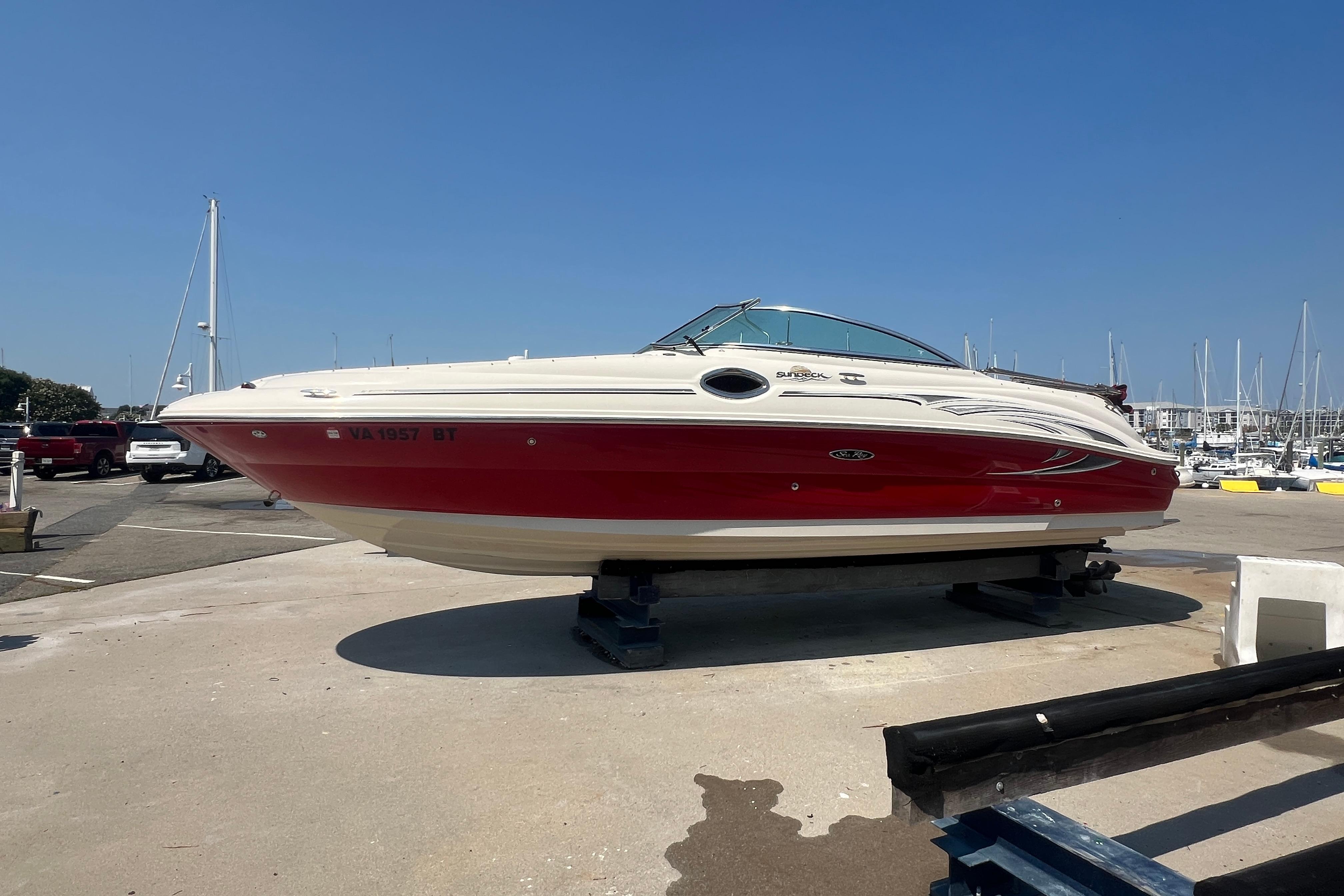 2005 Sea Ray 240 Sundeck boat with red hull, docked at a marina under clear blue sky.