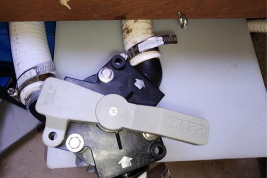 Marine plumbing valve on a 1985 Wasque Down East Cruiser, featuring hose connections and clamps.
