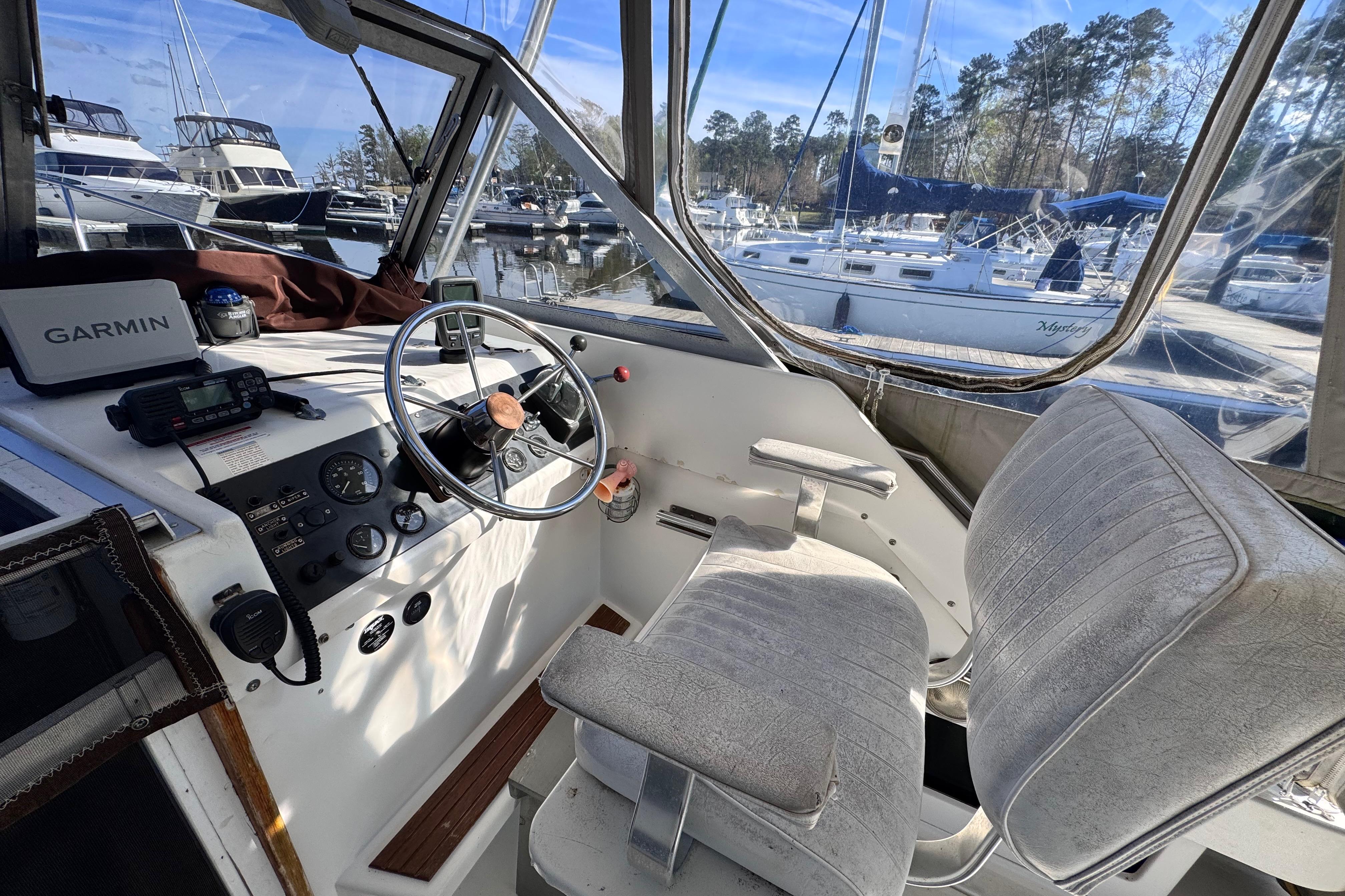 1987 Luhrs Alura 30 boat cockpit with steering wheel, Garmin device, and marina view.