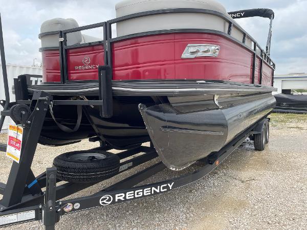 2023 Regency 250DL3 pontoon boat on trailer, red exterior, parked on gravel.