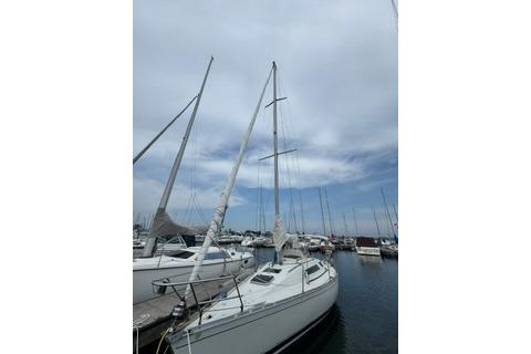 1986 Beneteau First 305 sailboat docked at a marina under a cloudy sky.