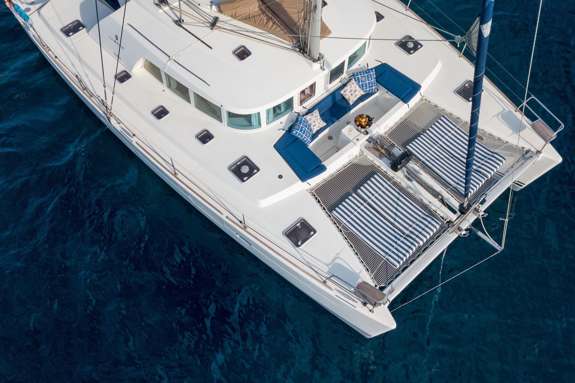 Aerial view of 2005 Lagoon 440 catamaran with blue cushions and striped nets on the ocean.