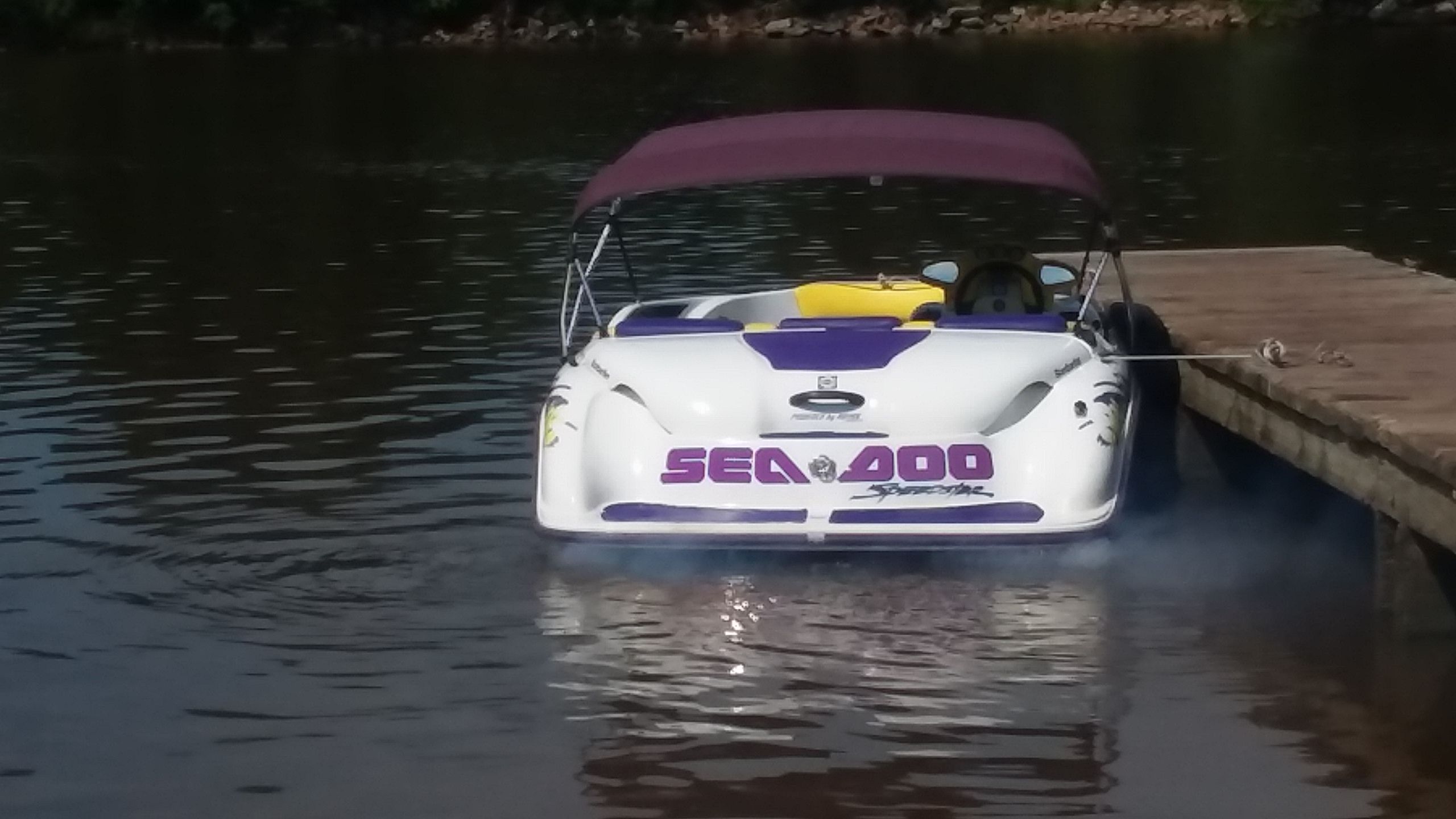 A white 1995 SeaDoo SPEEDSTER boat is docked at a wooden pier on the water.