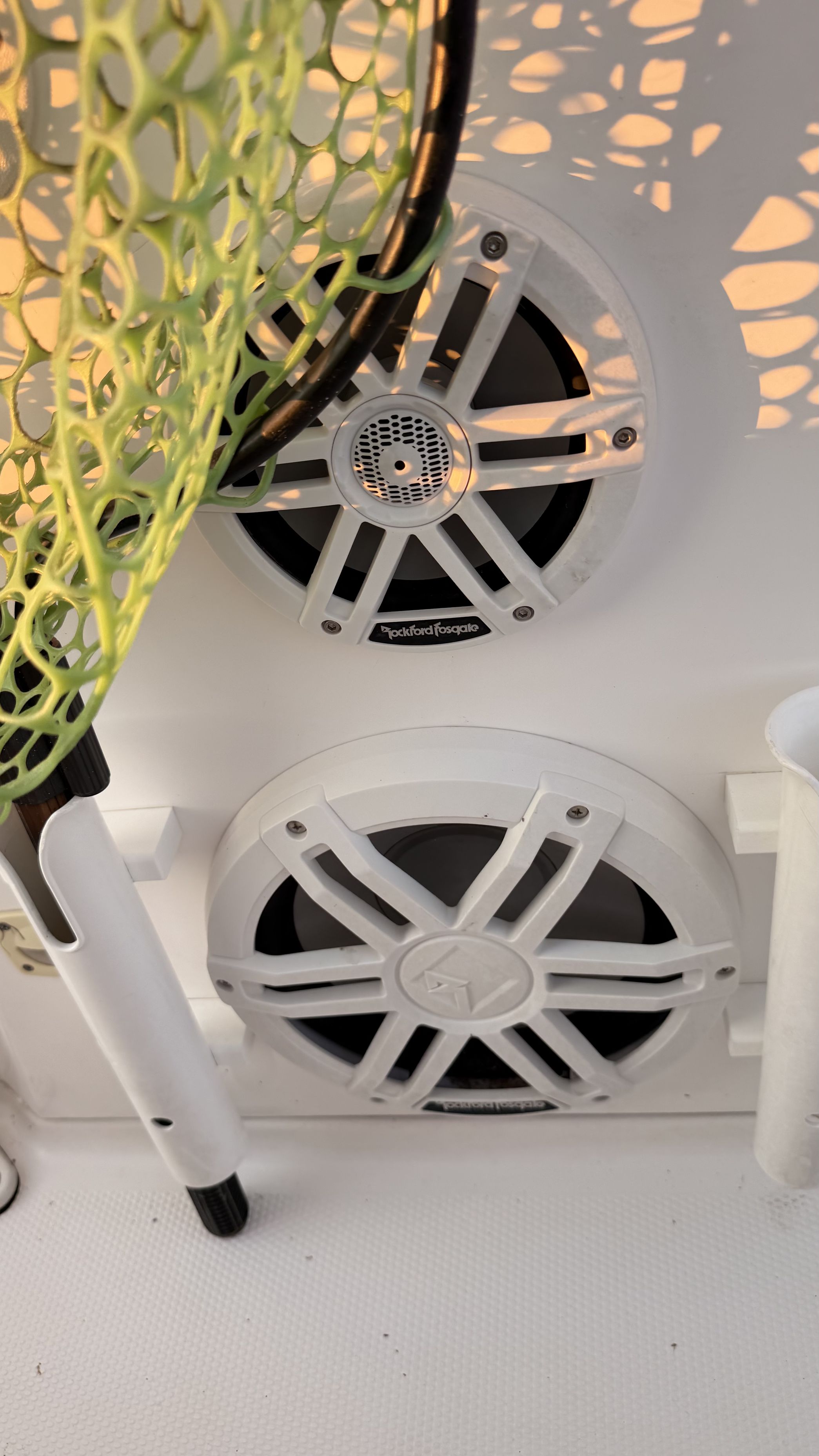 Two speakers are mounted on the white boat wall, with a green net and a holder nearby.