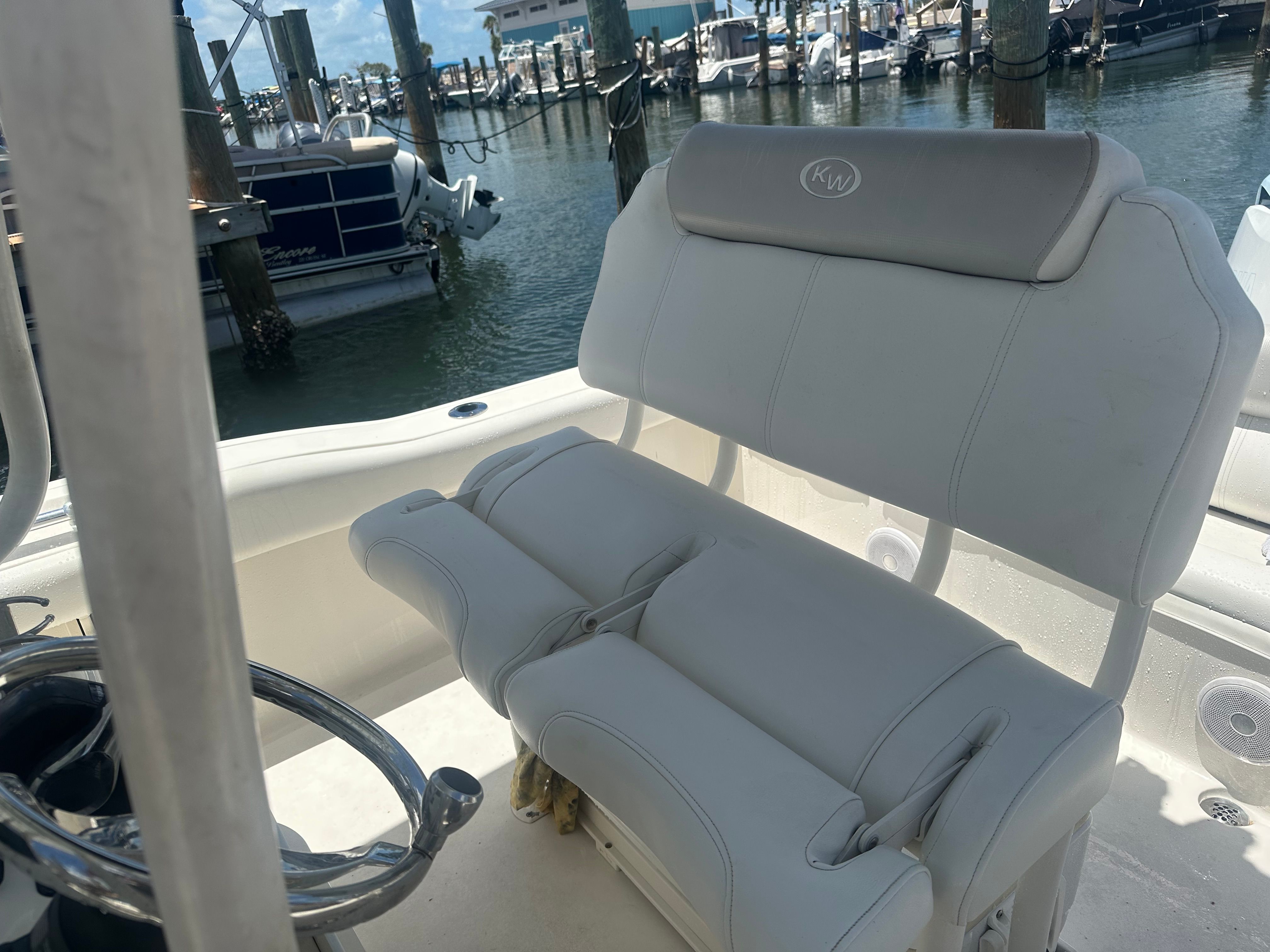A Key West 219 FS boat in a marina, featuring white seating and a steering wheel.