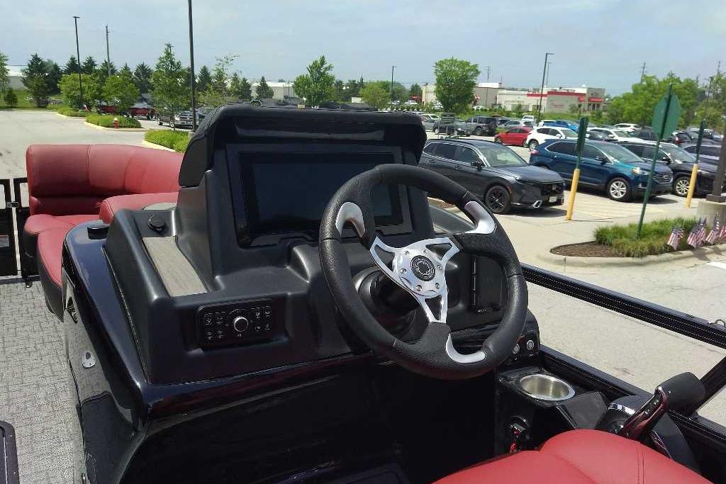 2026 Regency 230 DL boat dashboard with steering wheel and red seating in parking lot.
