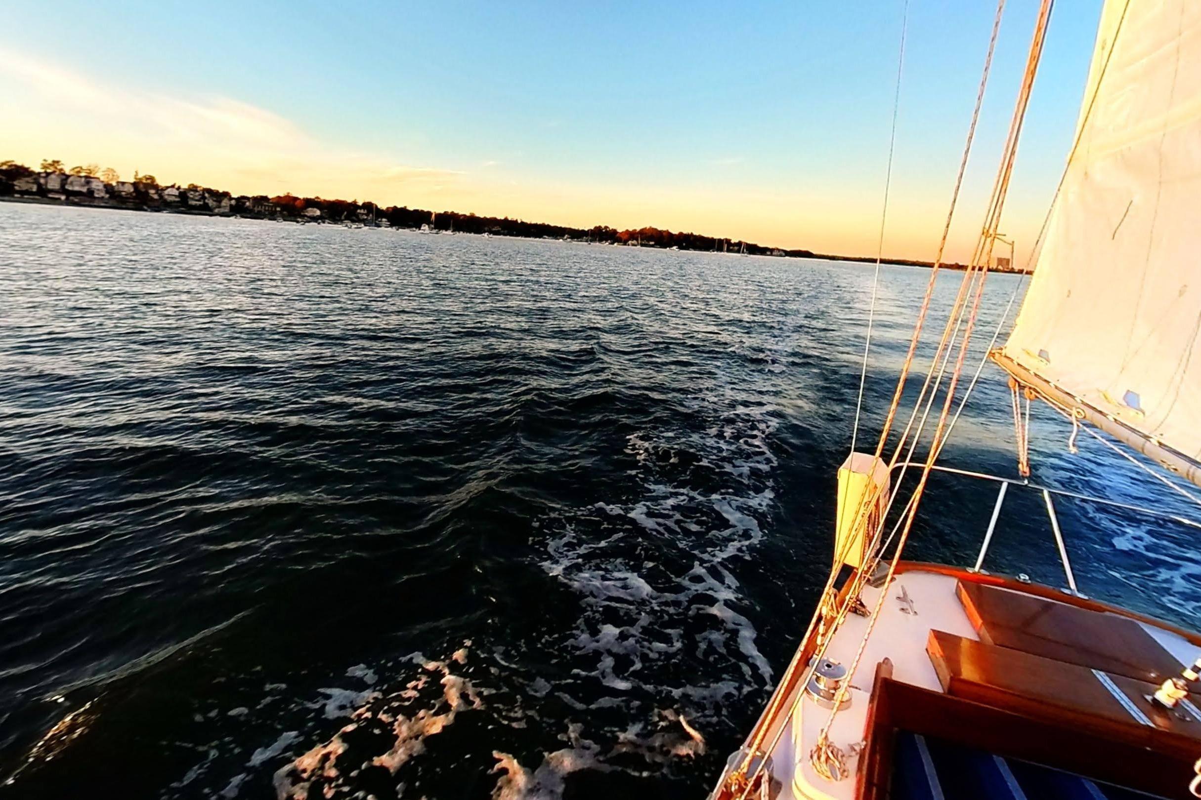 Sailing on a 1970 Hinckley Bermuda 40 at sunset, serene waters and distant shoreline.