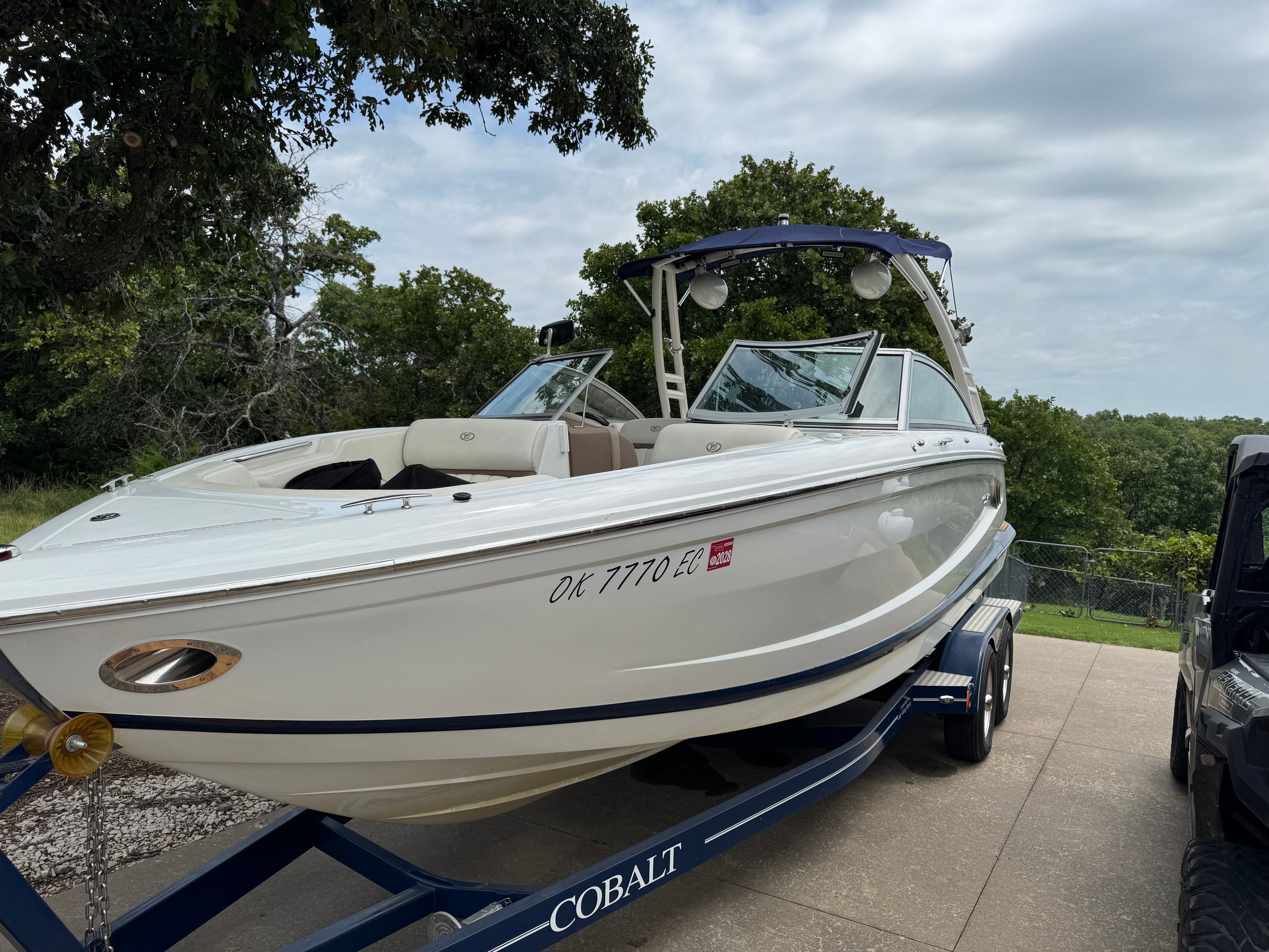 A white 2011 Cobalt A25 boat on a trailer, surrounded by trees.