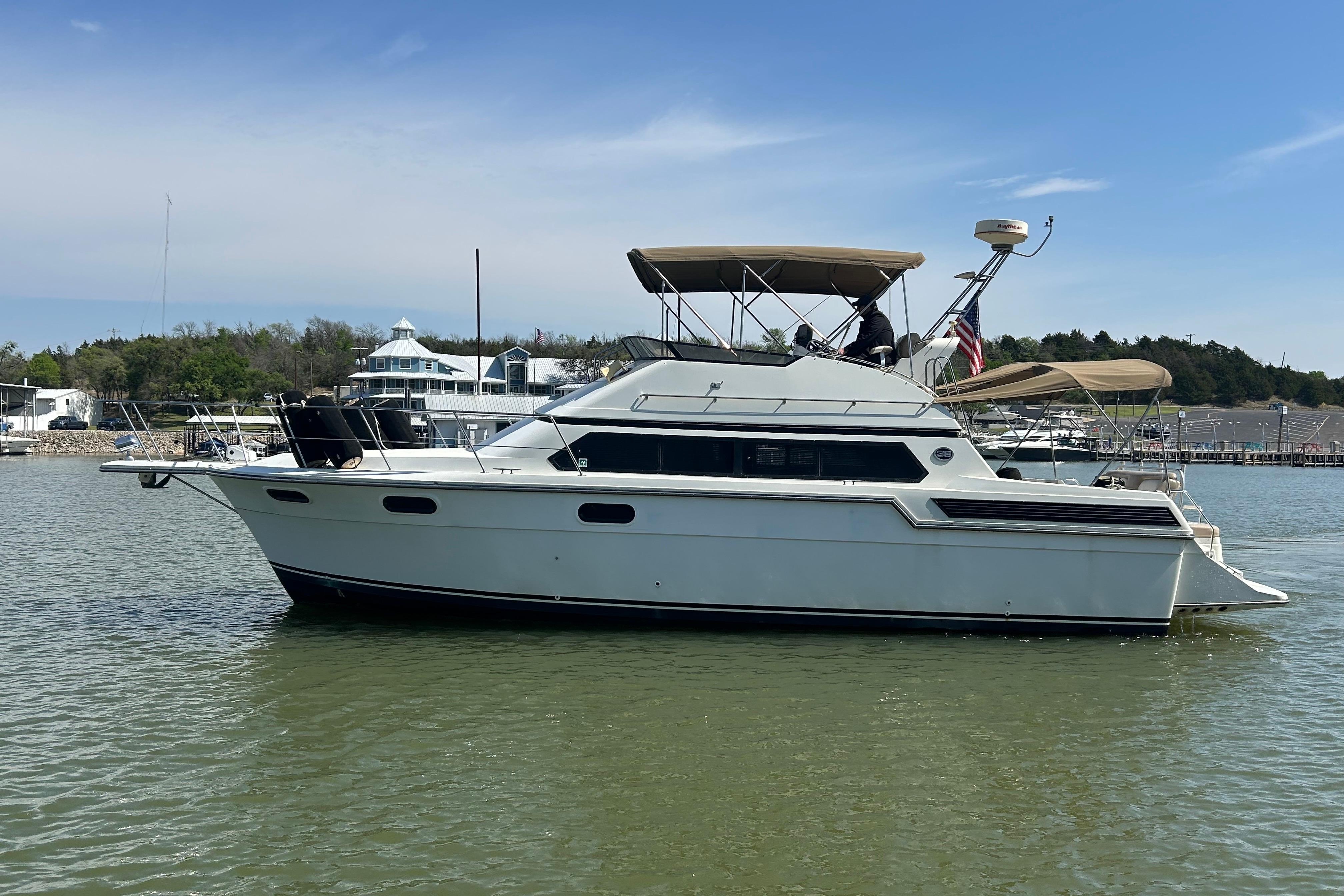 1989 Carver 380 Santego yacht on calm water, with marina and trees in the background.